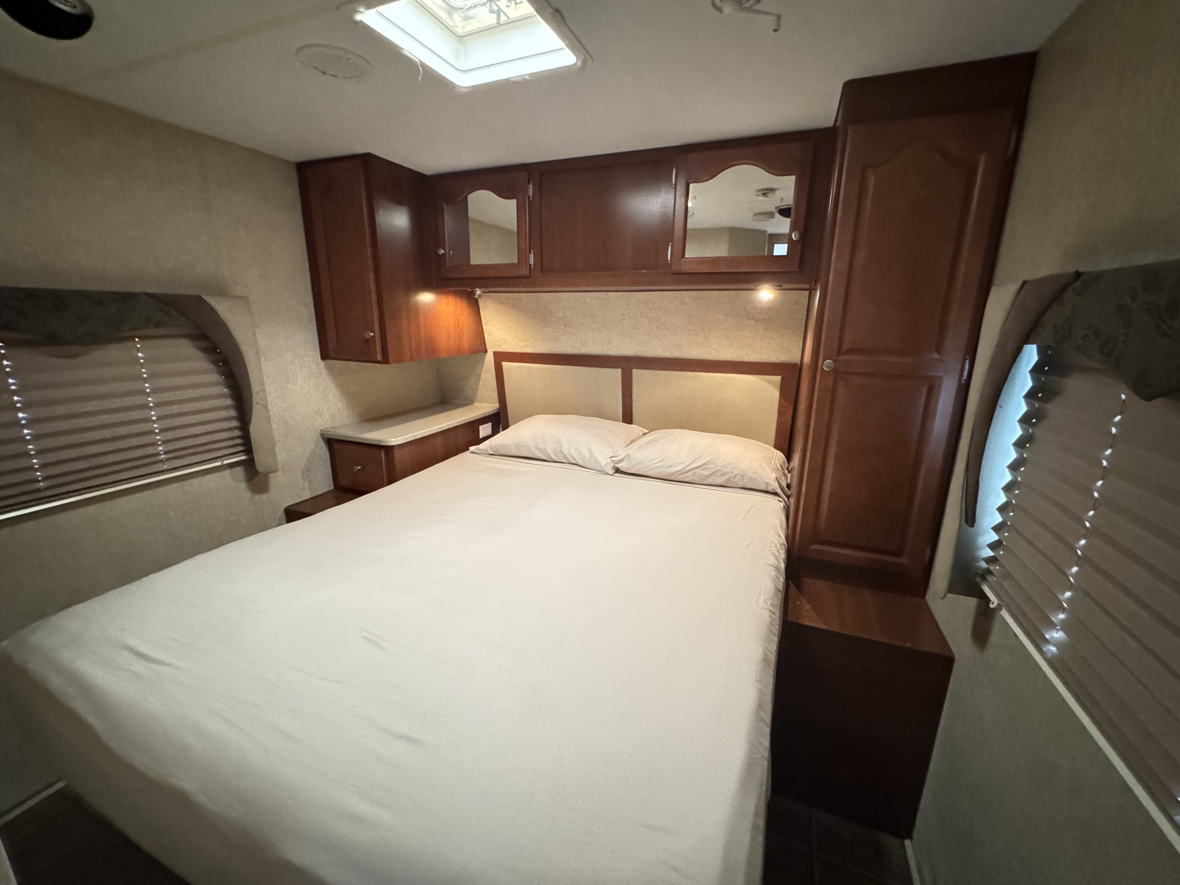 Cozy RV rental bedroom with a comfortable bed, wooden cabinets, and window blinds. Features a ceiling skylight.. Fleetwood Prowler 2009