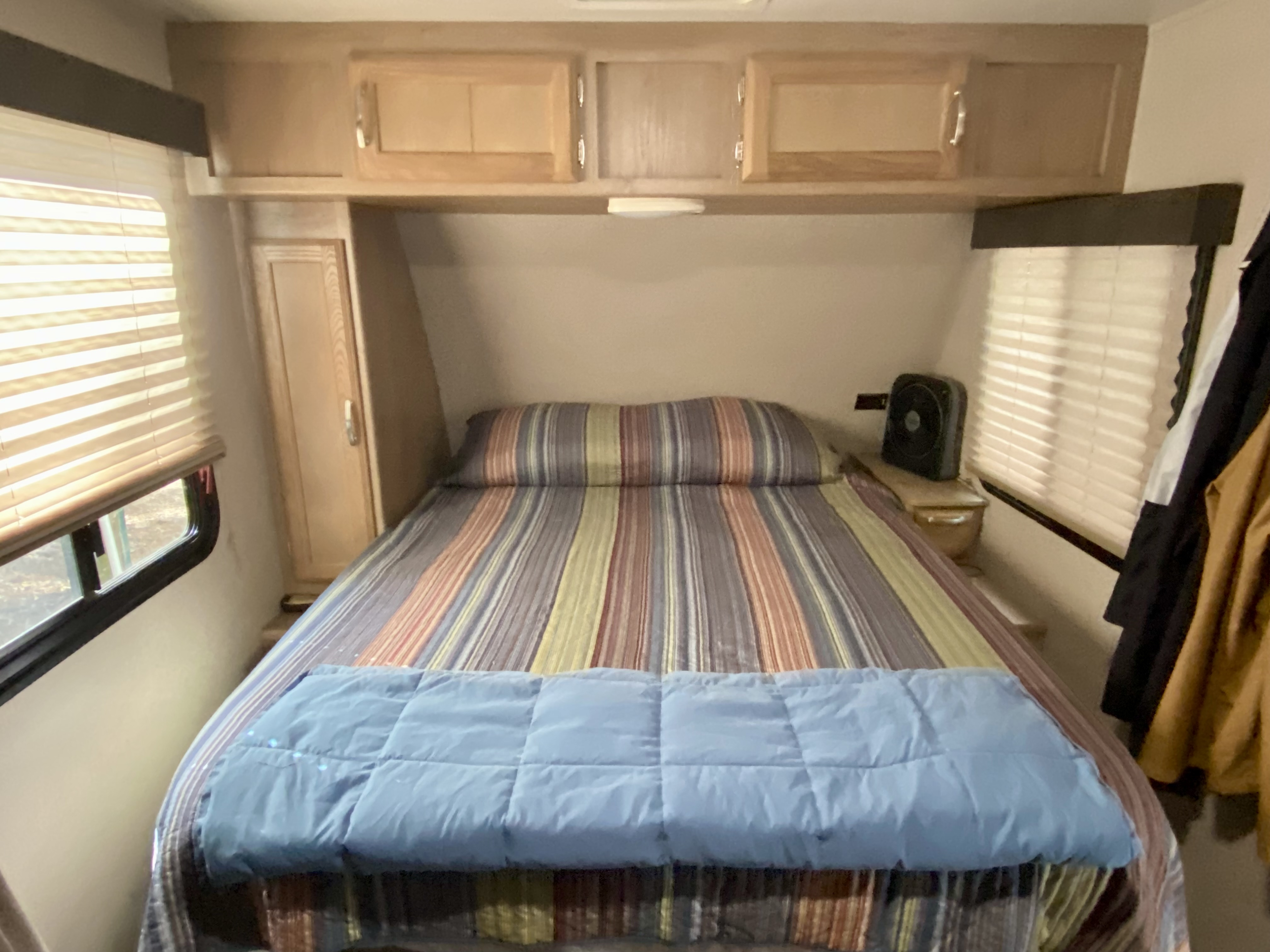 Cozy RV rental bedroom with striped bedding, overhead cabinets, and windows with blinds.. Winnebago Minnie Winnie 2020