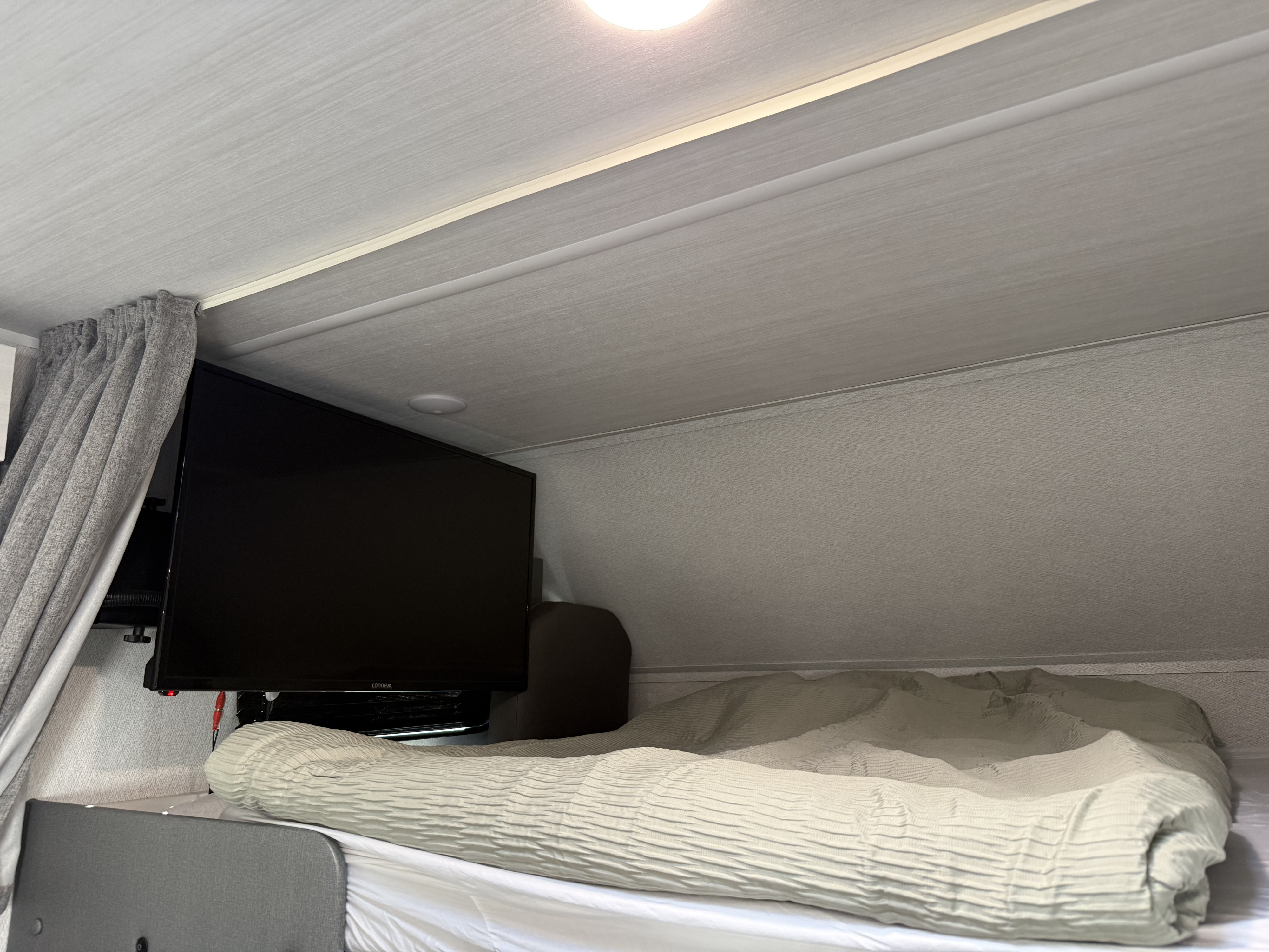 Inside an RV rental: a cozy sleeping area features a bed with a light textured comforter and a mounted TV.. Forest River ENTRADA 3100FB 2024