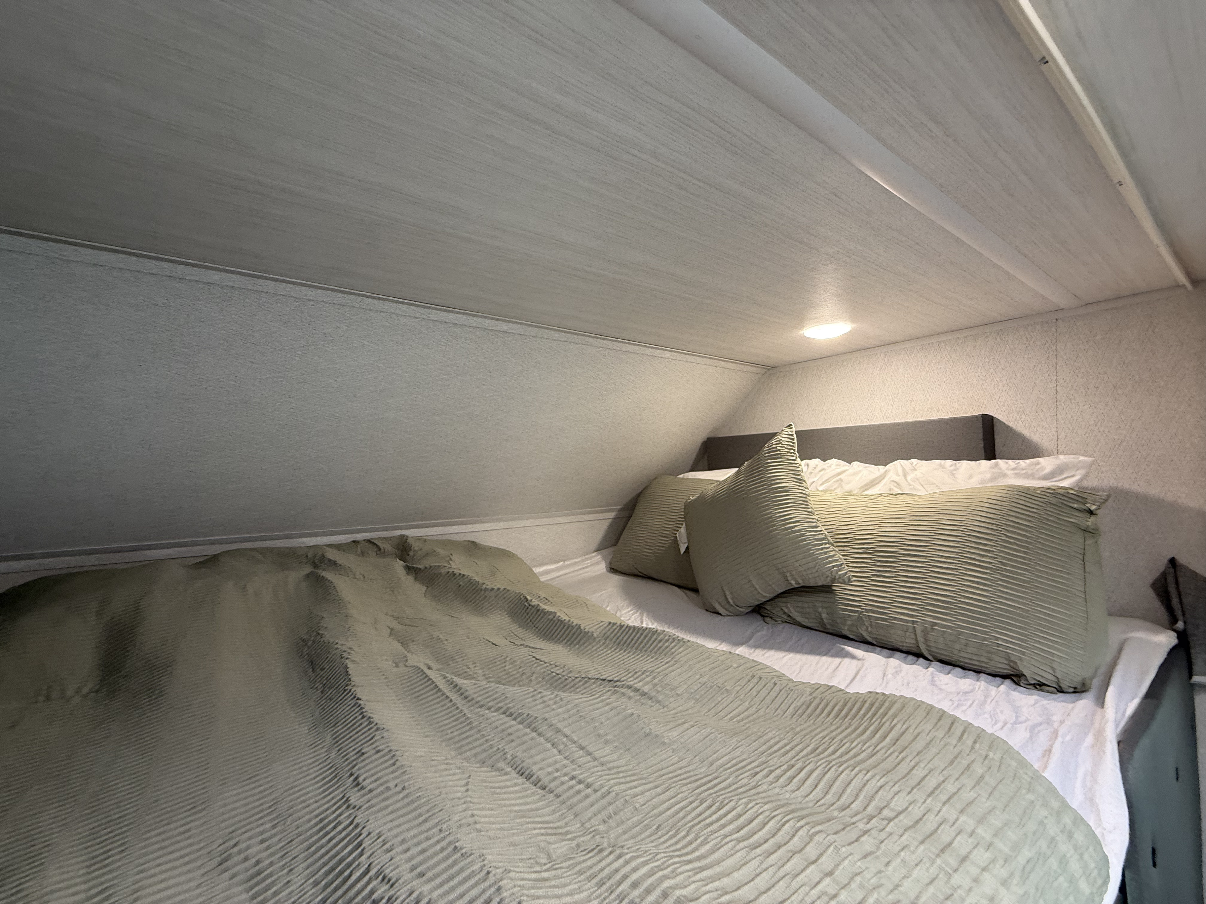 RV rental's cozy sleeping area with light green textured bedding, pillows, and an upholstered headboard. Recessed light.. Forest River ENTRADA 3100FB 2024