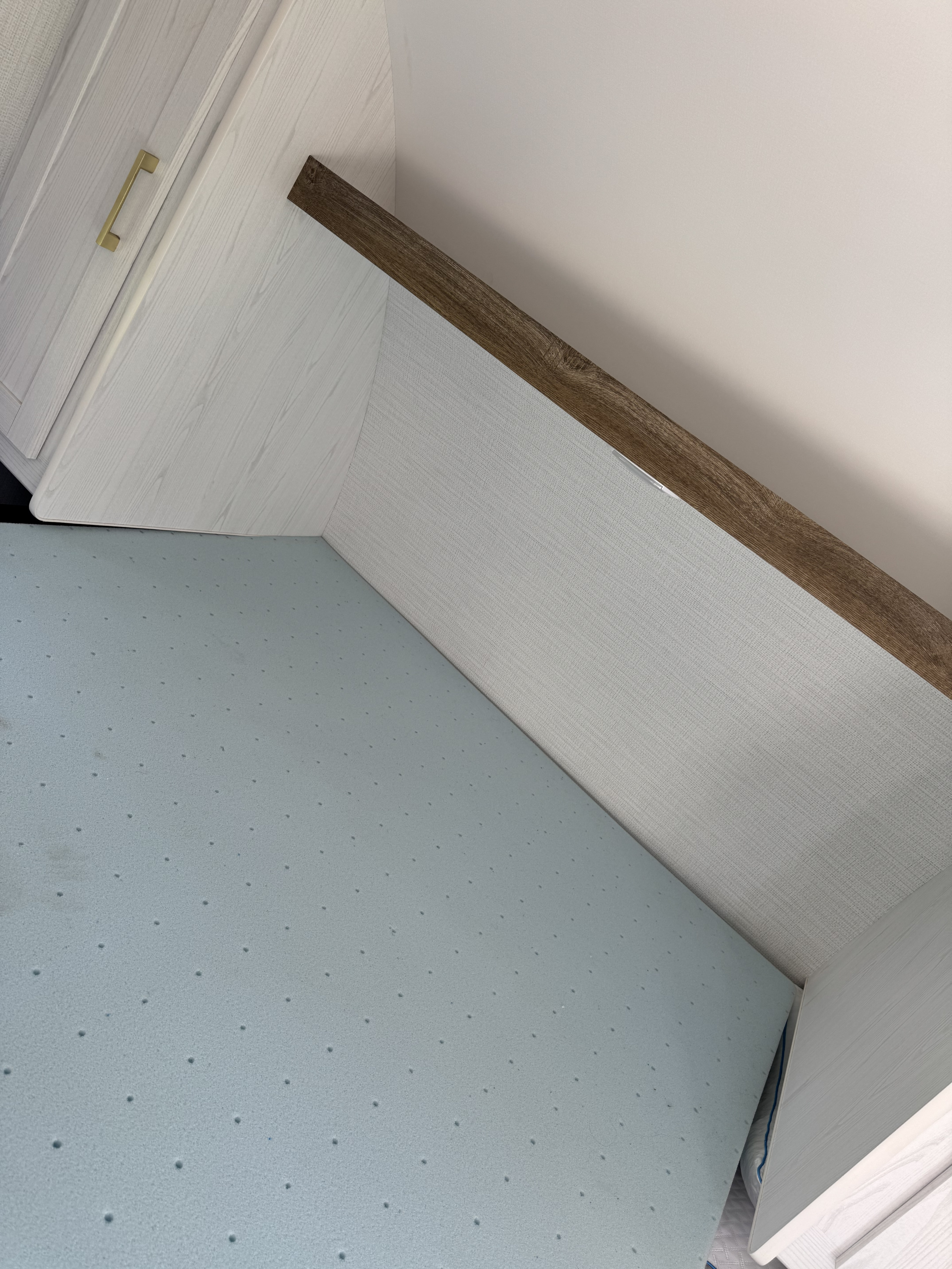 Inside an RV rental: light blue perforated foam mattress, light wood cabinet with gold handle, textured wall.. Heartland RVs 210RD-C 2024