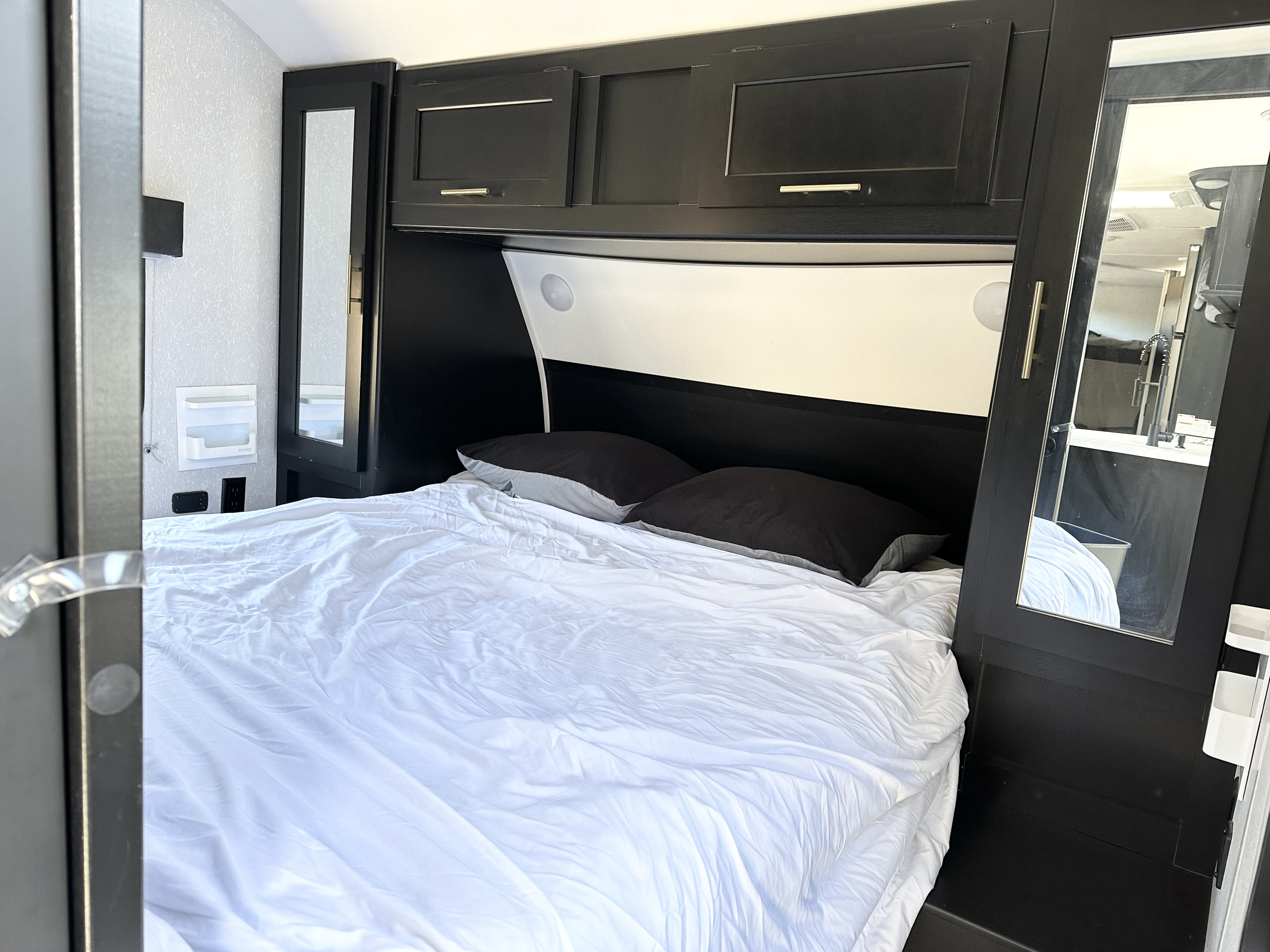 Spacious RV rental bedroom featuring a large bed with white bedding, black cabinetry, and mirrored closet doors.. Forest River Cherokee Grey Wolf 2021