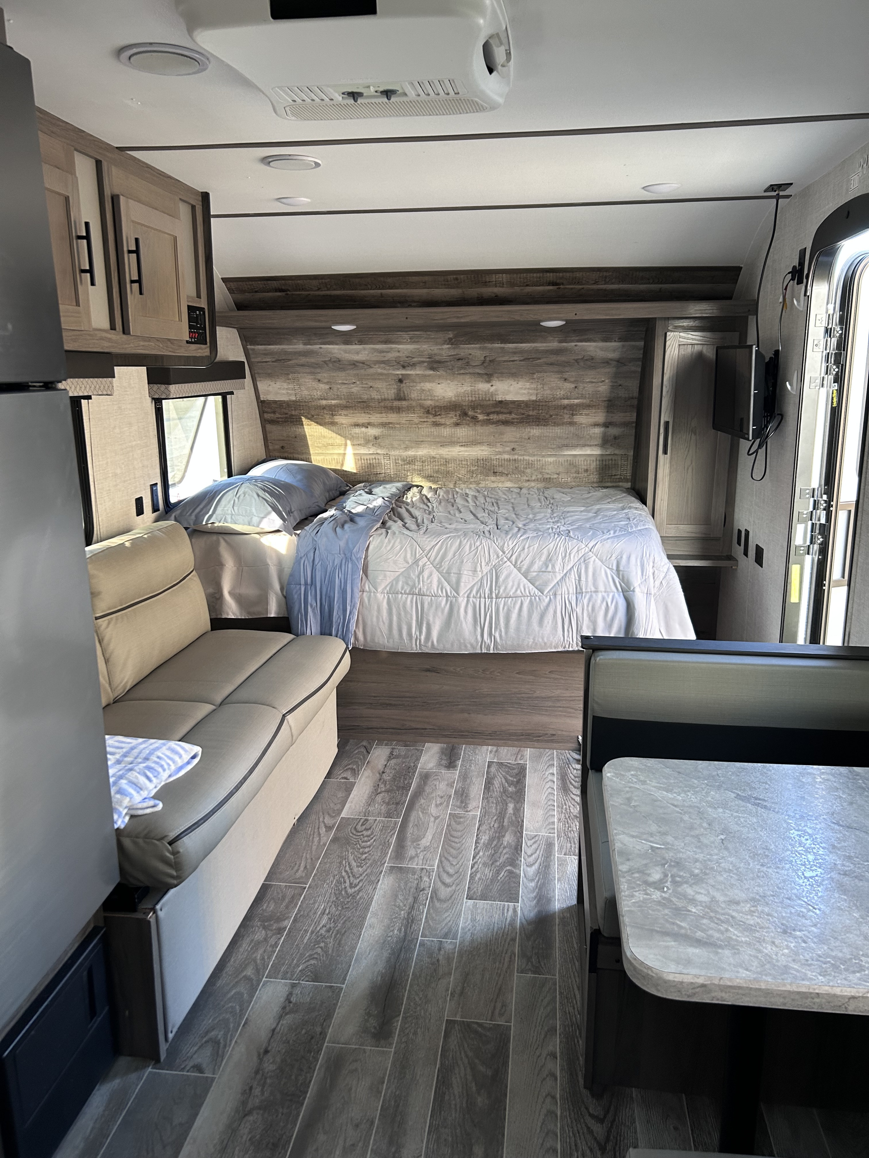 Spacious RV rental interior featuring a queen bed, sofa, and dining booth with wood-look flooring and modern cabinets.. Gulf Stream Ameri-Lite 2022