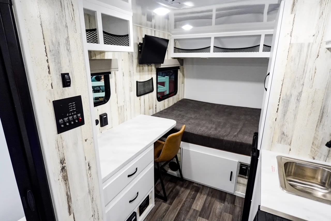Functional RV rental interior featuring a comfortable bed, work desk, TV, and compact kitchen area for travel.. Modern Buggy RV Country Born CB16 2025