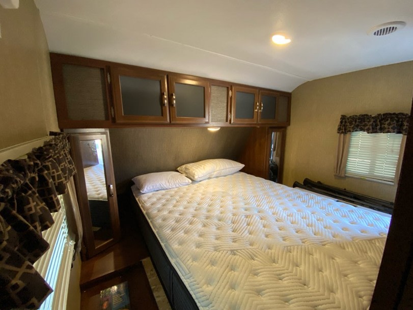 Cozy RV rental bedroom with a white mattress, wood cabinets, and window. Ideal for comfortable travel.. Keystone RV Passport Grand Touring 2017