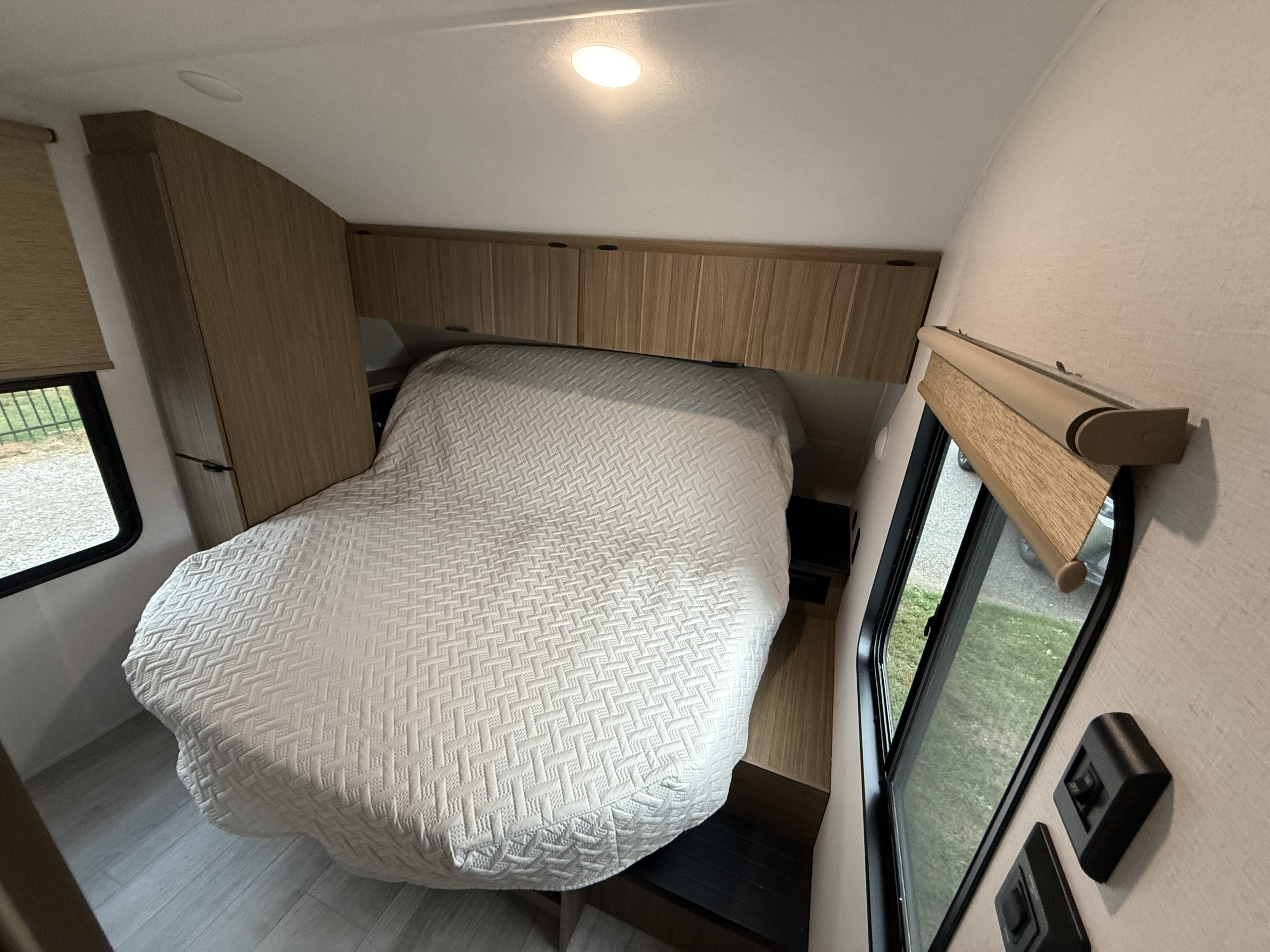View of an RV rental bedroom with a comfy bed, overhead storage, and natural light from windows.. Forest River Wildwood 2025