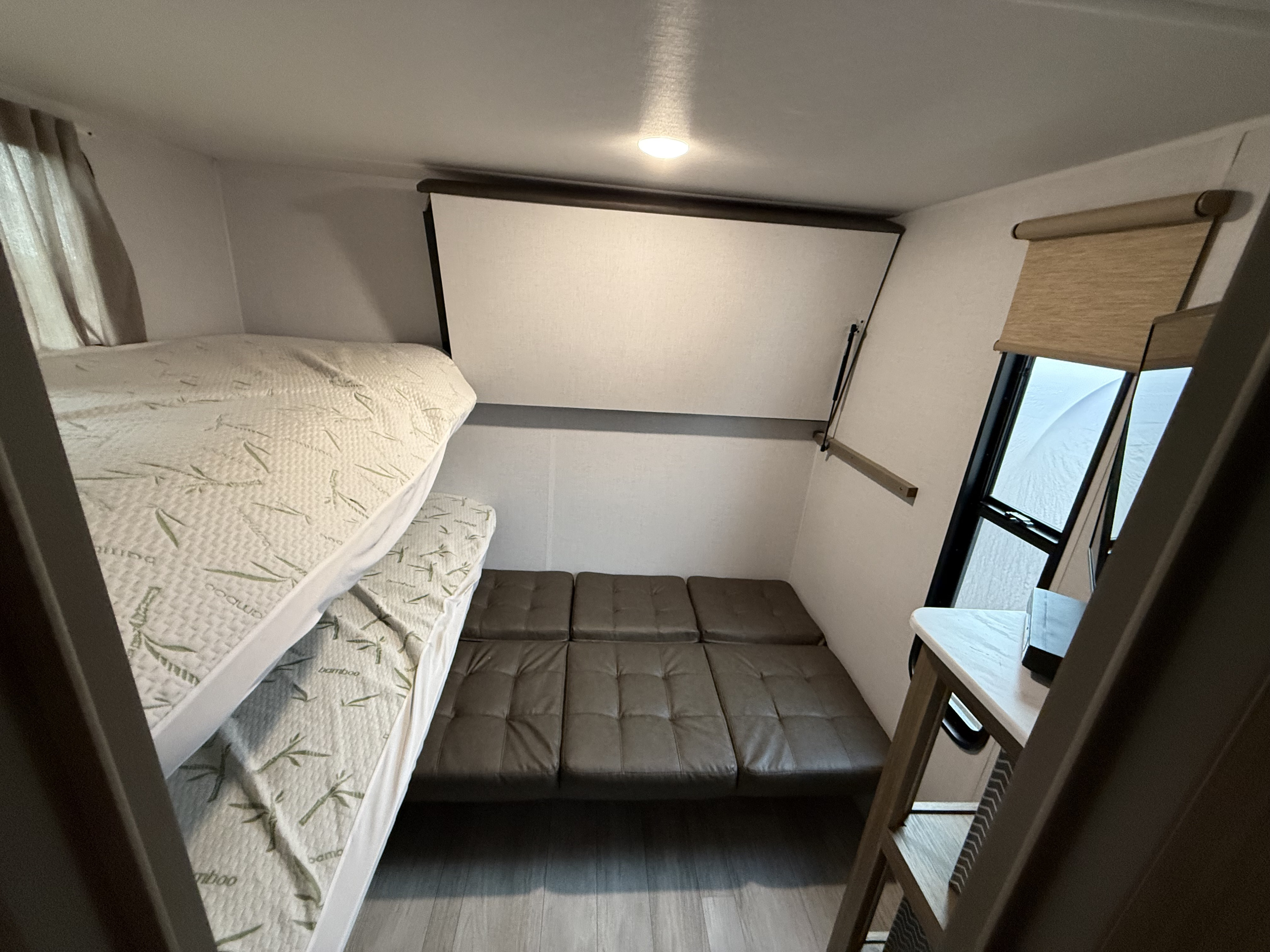 RV rental interior: two bunk beds with bamboo print mattresses & a brown convertible sofa. Compact, versatile sleeping/living area.. Forest River Wildwood 2025