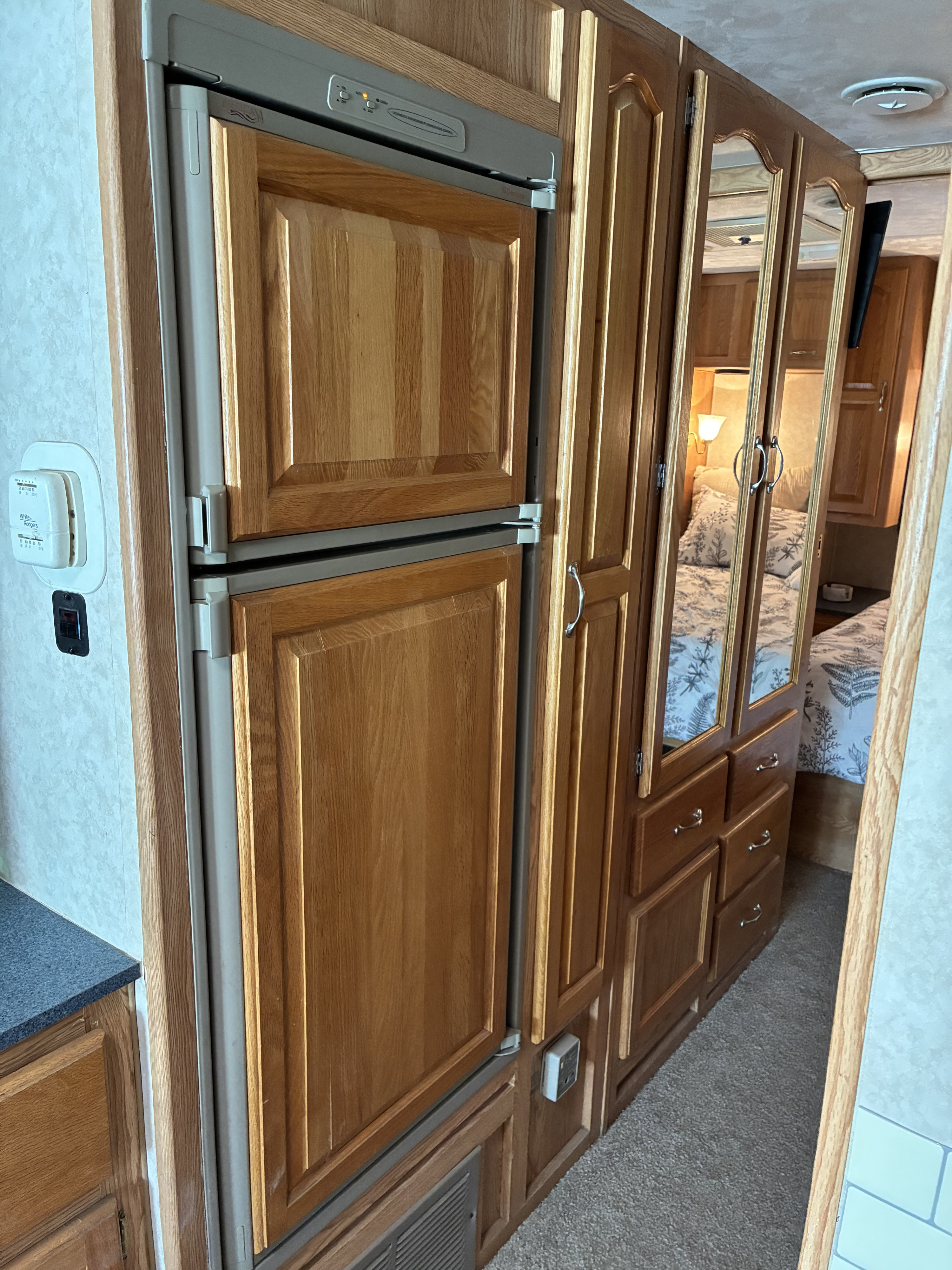 RV rental interior: A wood-paneled refrigerator, mirrored cabinets reflecting a cozy bedroom, and a thermostat on the wall.. Damon Corporation Daybreak 2001