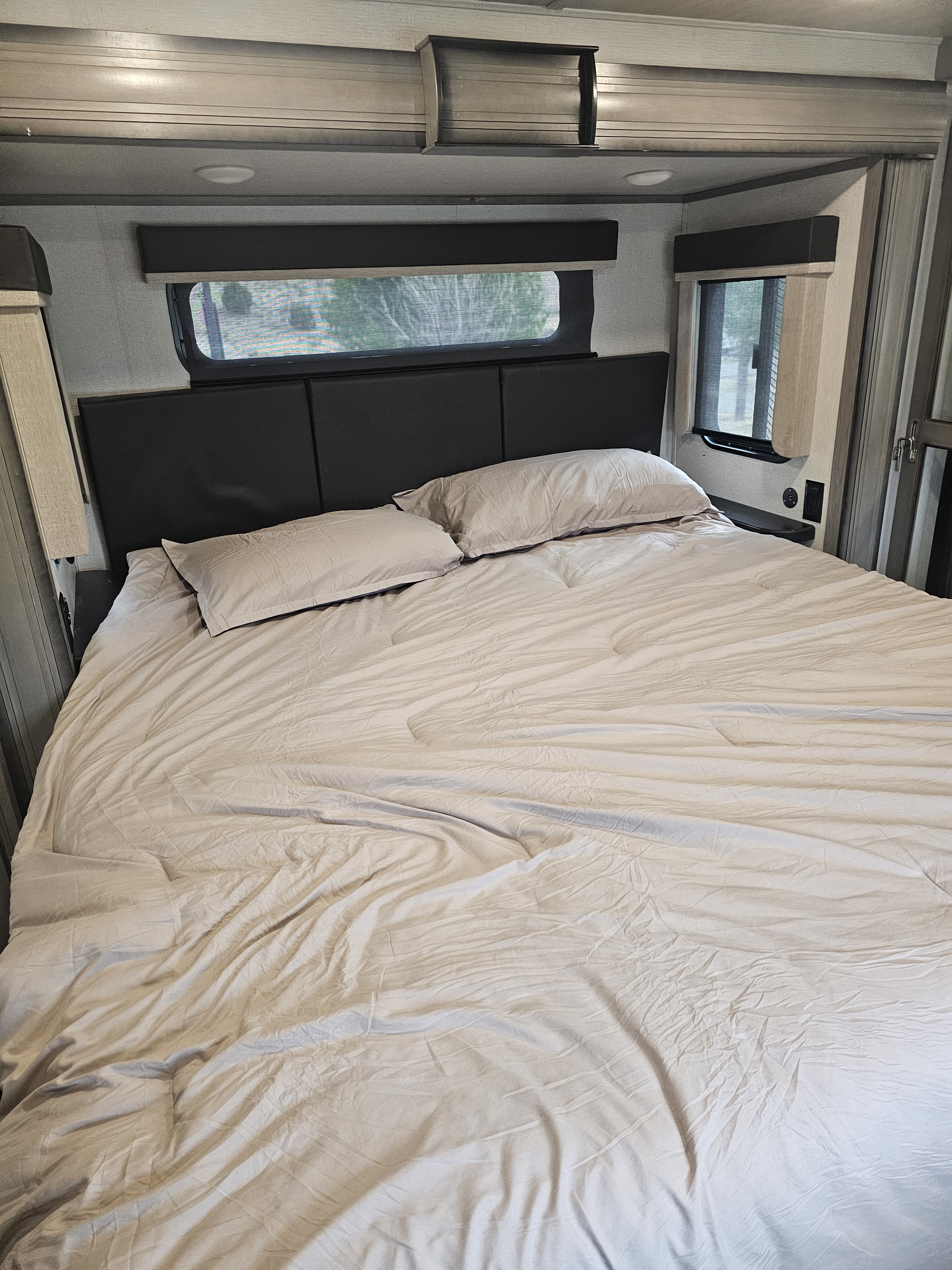 Spacious RV rental bedroom featuring a neat but used large bed with light-colored sheets, pillows, and functional window blinds.. Keystone RV Montana 2021