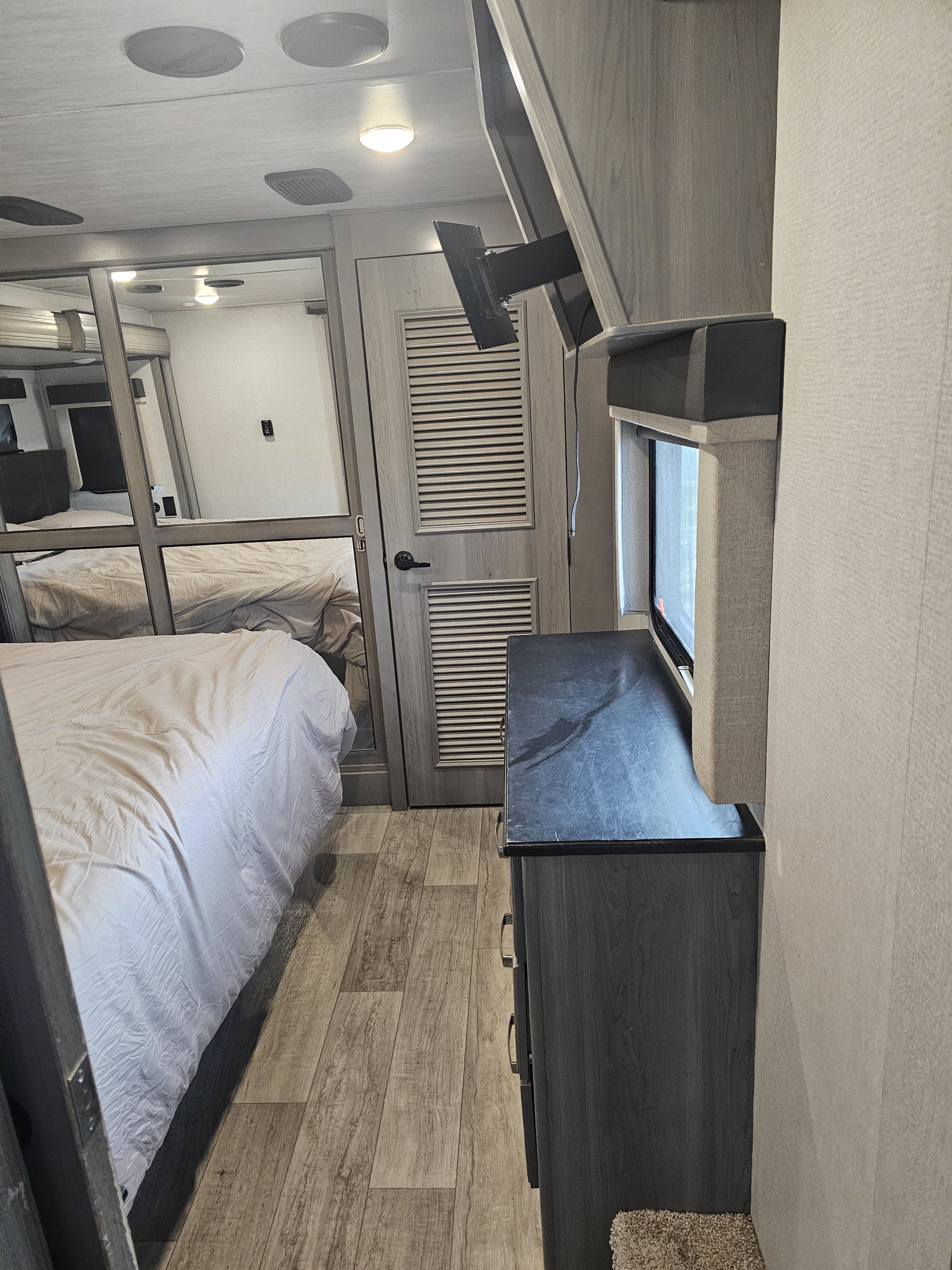 Modern RV rental bedroom with a comfy bed, mirrored closet, dresser, and window, offering a bright and inviting space.. Keystone RV Montana 2021