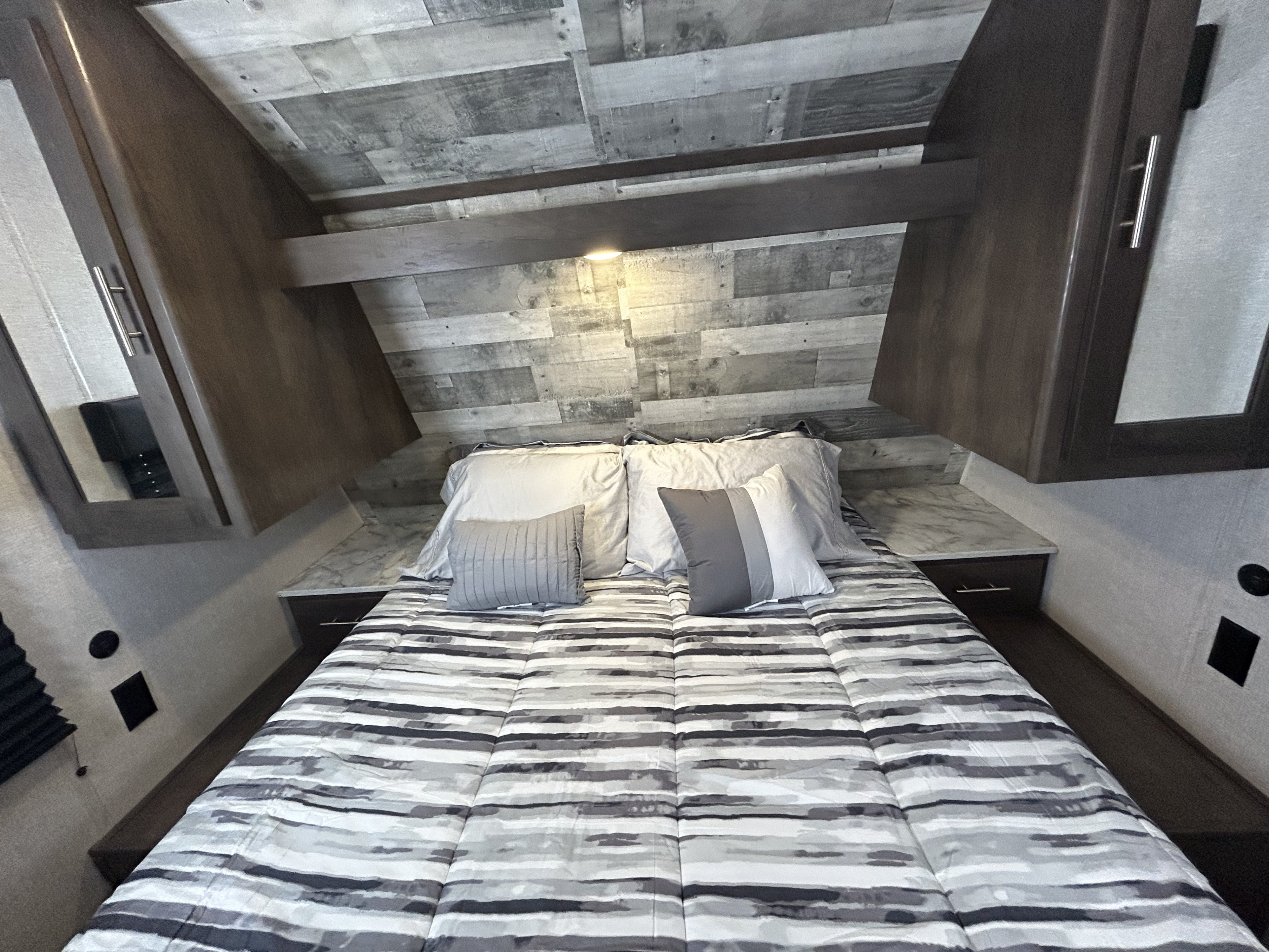 Cozy RV rental bedroom with a striped comforter, overhead storage, nightstands, and modern wood paneling.. Dutchmen Coleman Lantern 2021