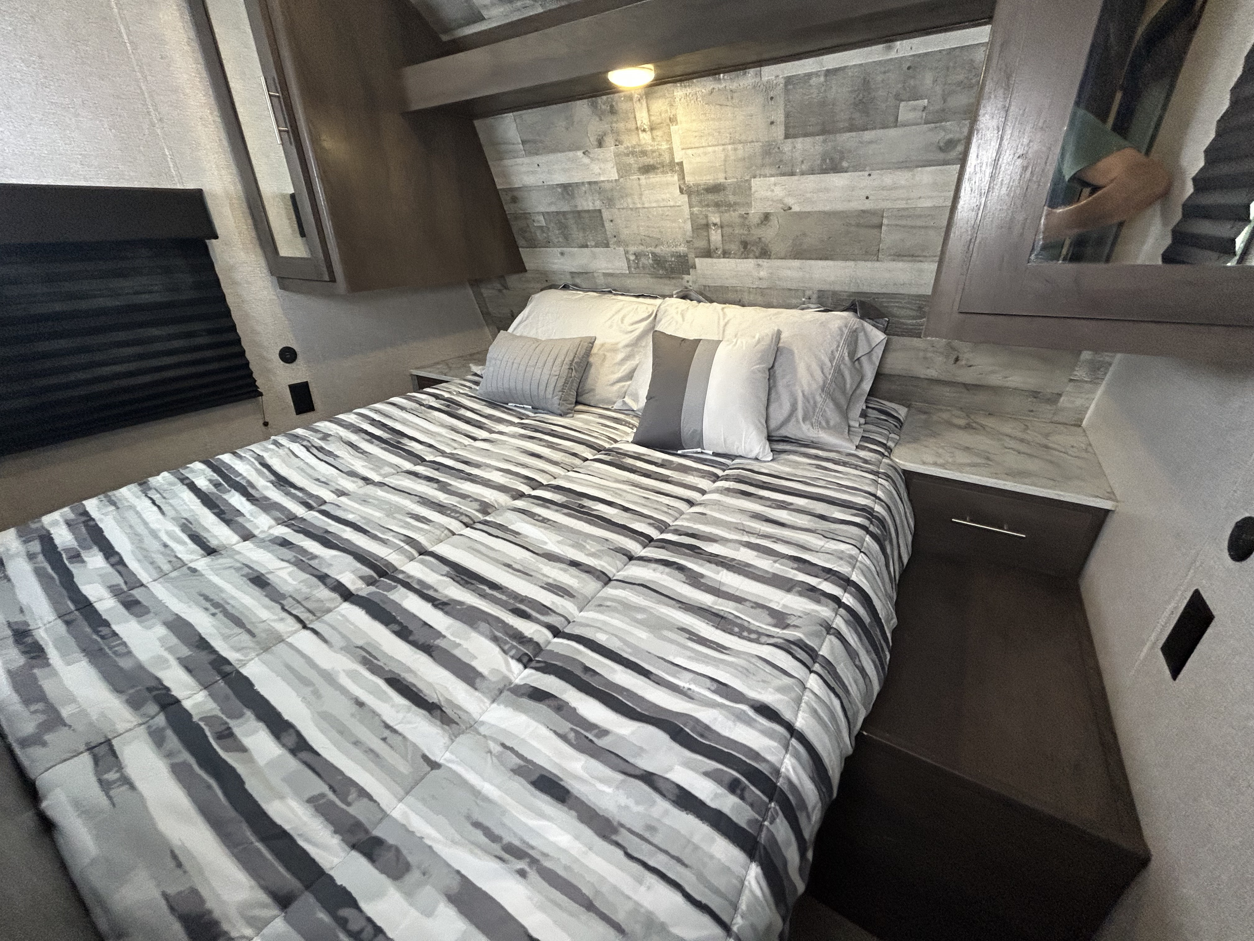 Cozy RV rental bedroom with a modern striped comforter and wood-paneled accent wall, perfect for travel comfort.. Dutchmen Coleman Lantern 2021
