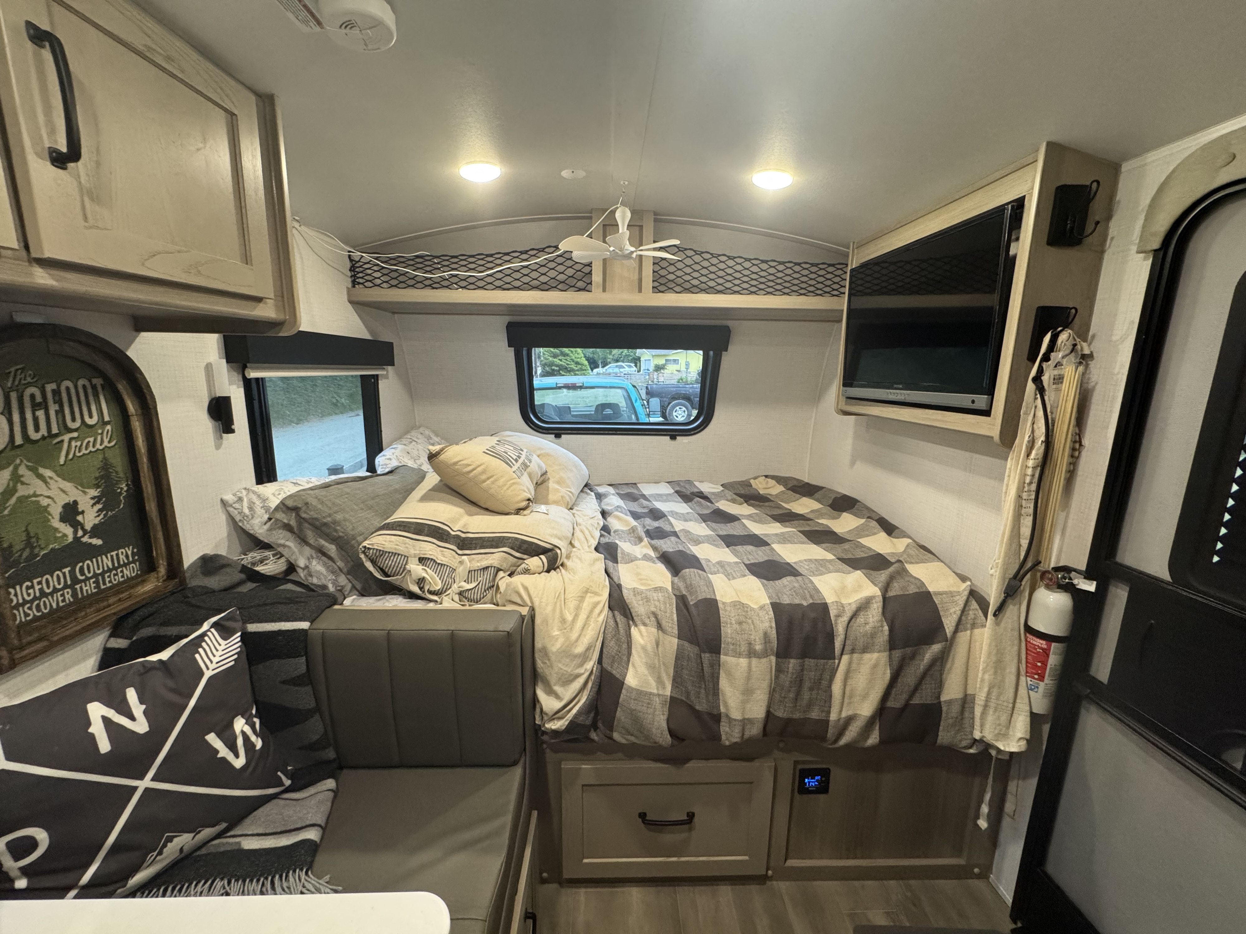 Cozy RV rental bedroom with a plaid bed, seating, overhead storage, TV, and a fire extinguisher for safety.. Forest River Flagstaff E-Pro 2024