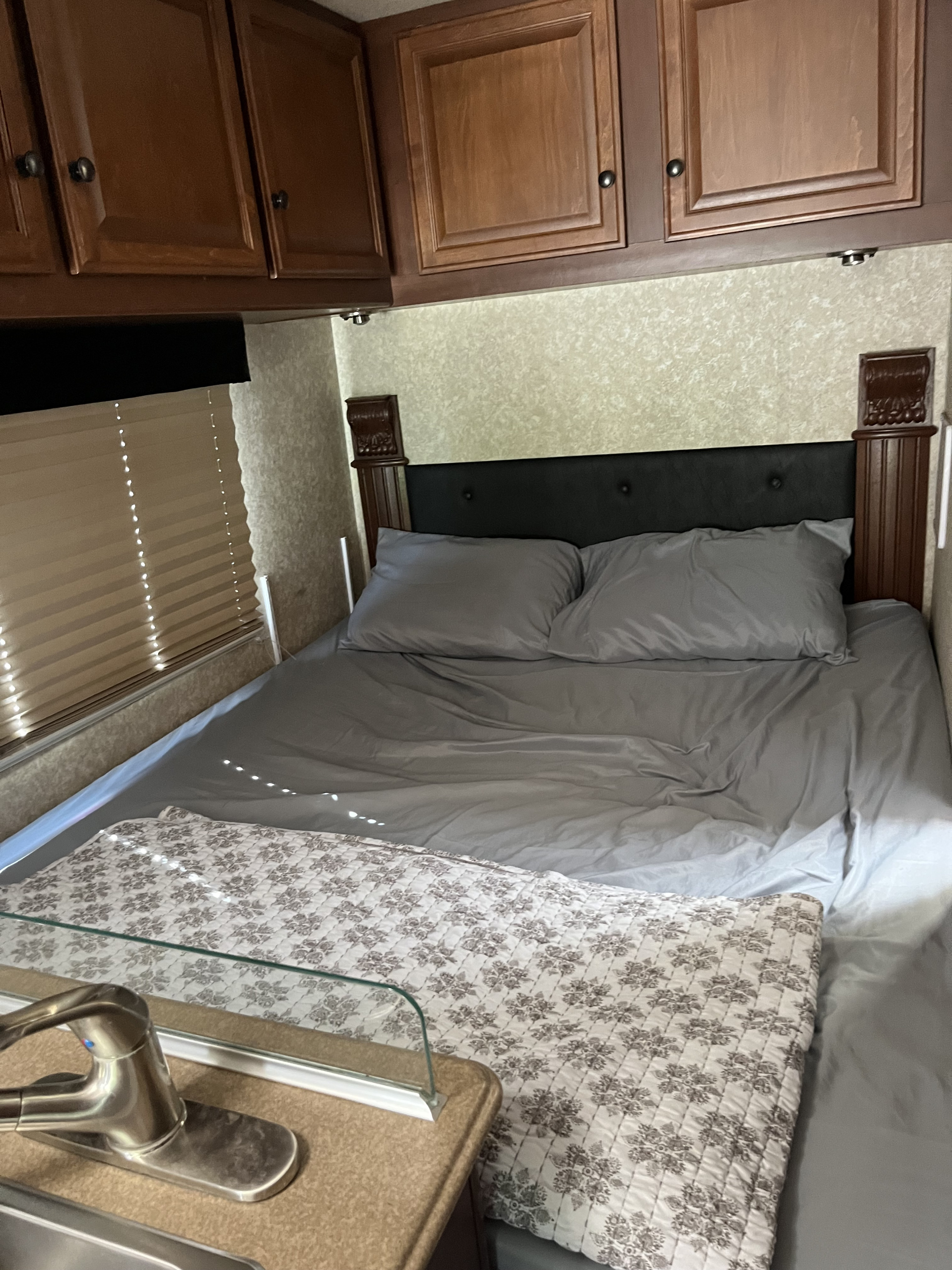 This RV rental's bedroom offers a comfortable grey bed, storage cabinets, and a window, with a partial view of a sink.. Tioga Montara 2012