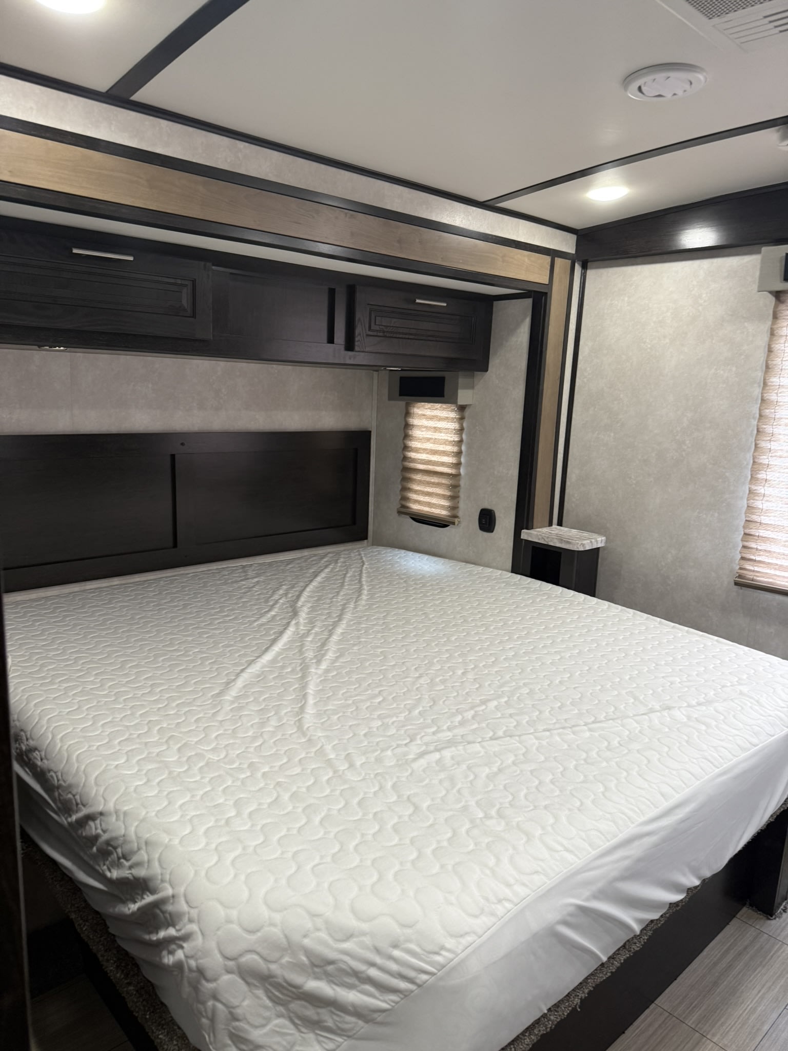 Spacious, clean RV rental bedroom with a large, inviting bed, dark wood headboard, and convenient overhead cabinets.. Forest River FR3 2019