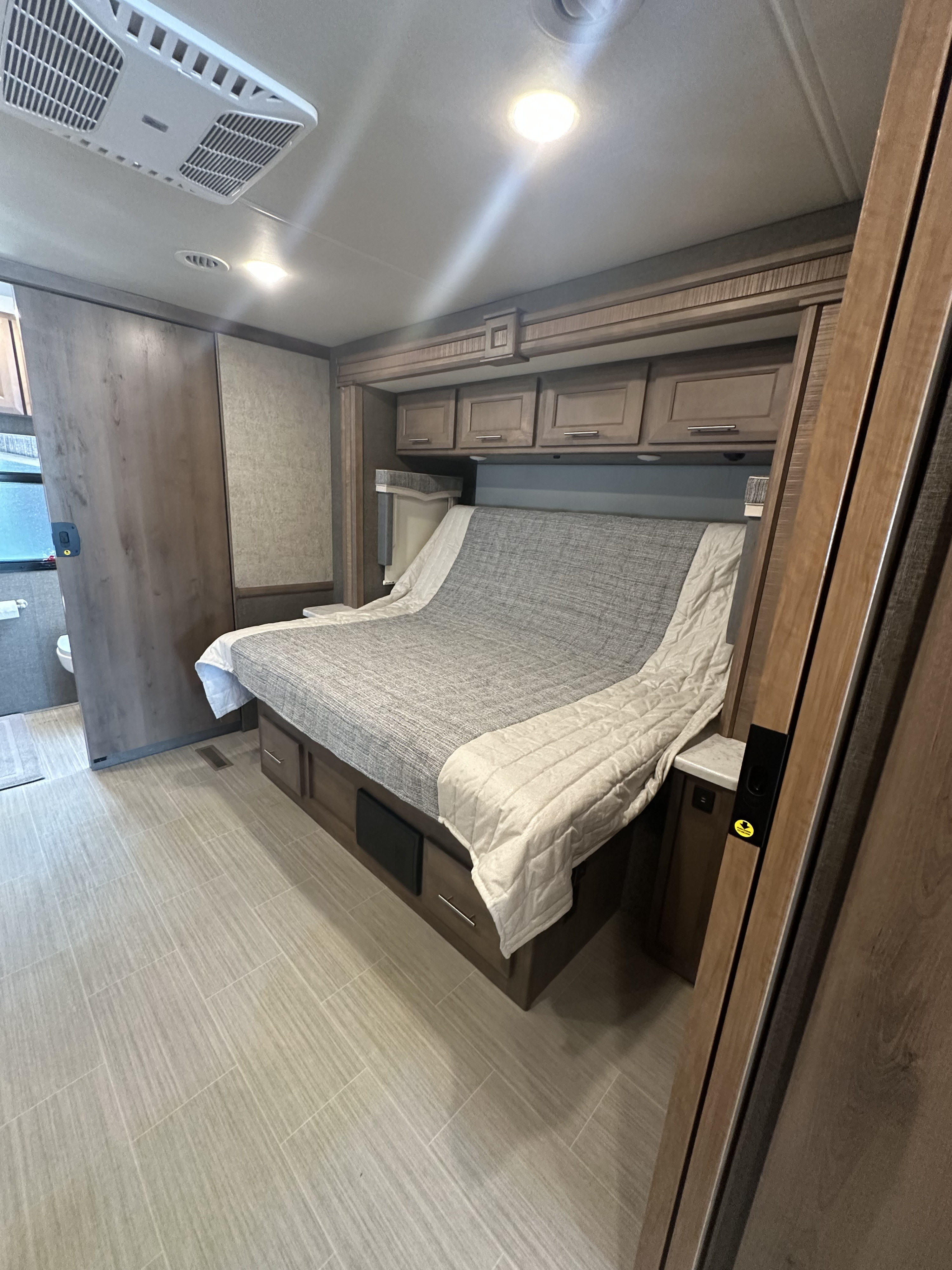 RV rental: Bedroom with a comfortable bed, wood cabinets, light tile floor, AC unit, and bathroom access.. Thor Challenger 2022