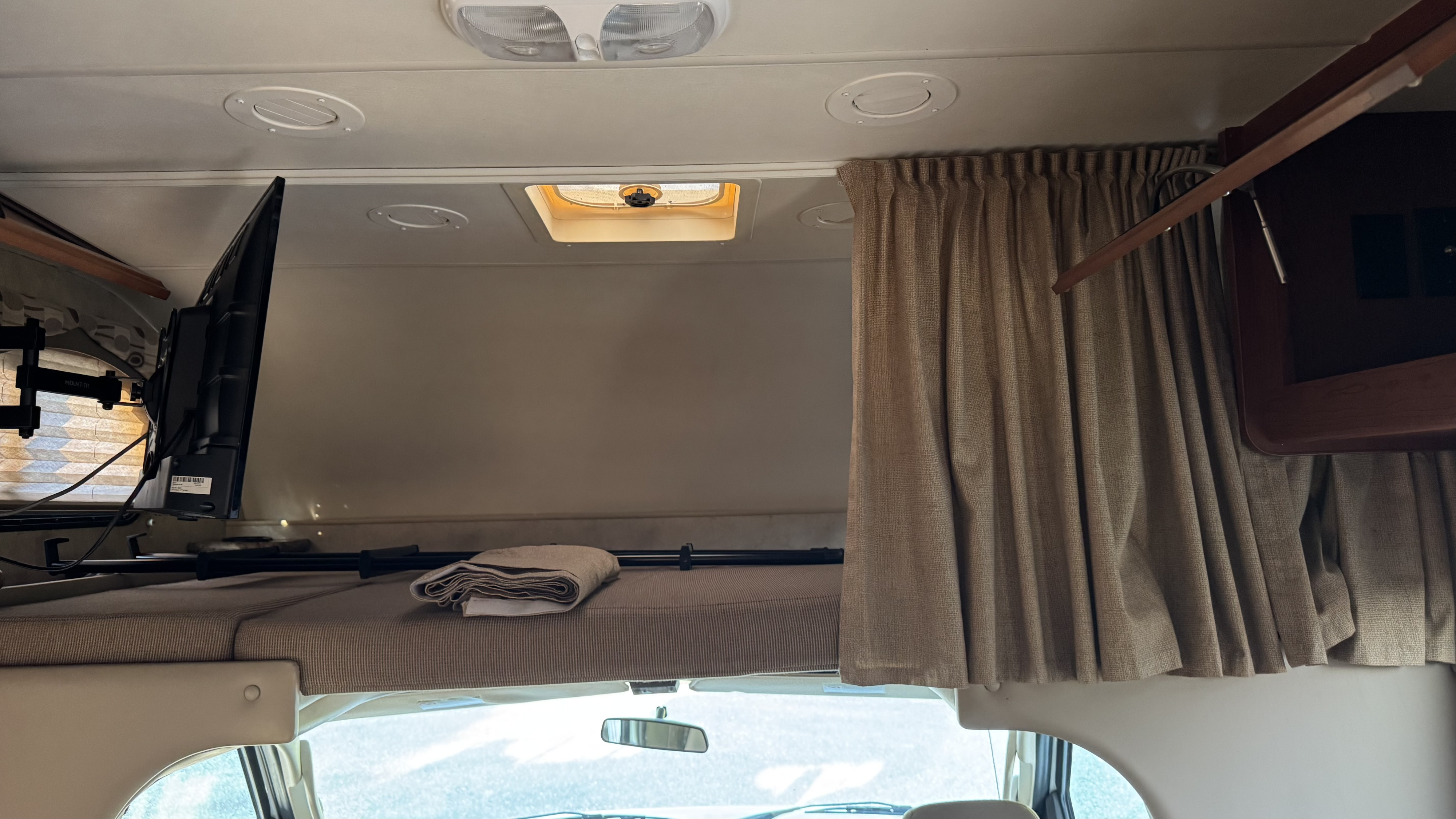 Inside an RV rental: the cozy over-cab bunk features a mounted TV, curtains, and a roof vent, providing a sleeping space.. Thor Chateau 2012