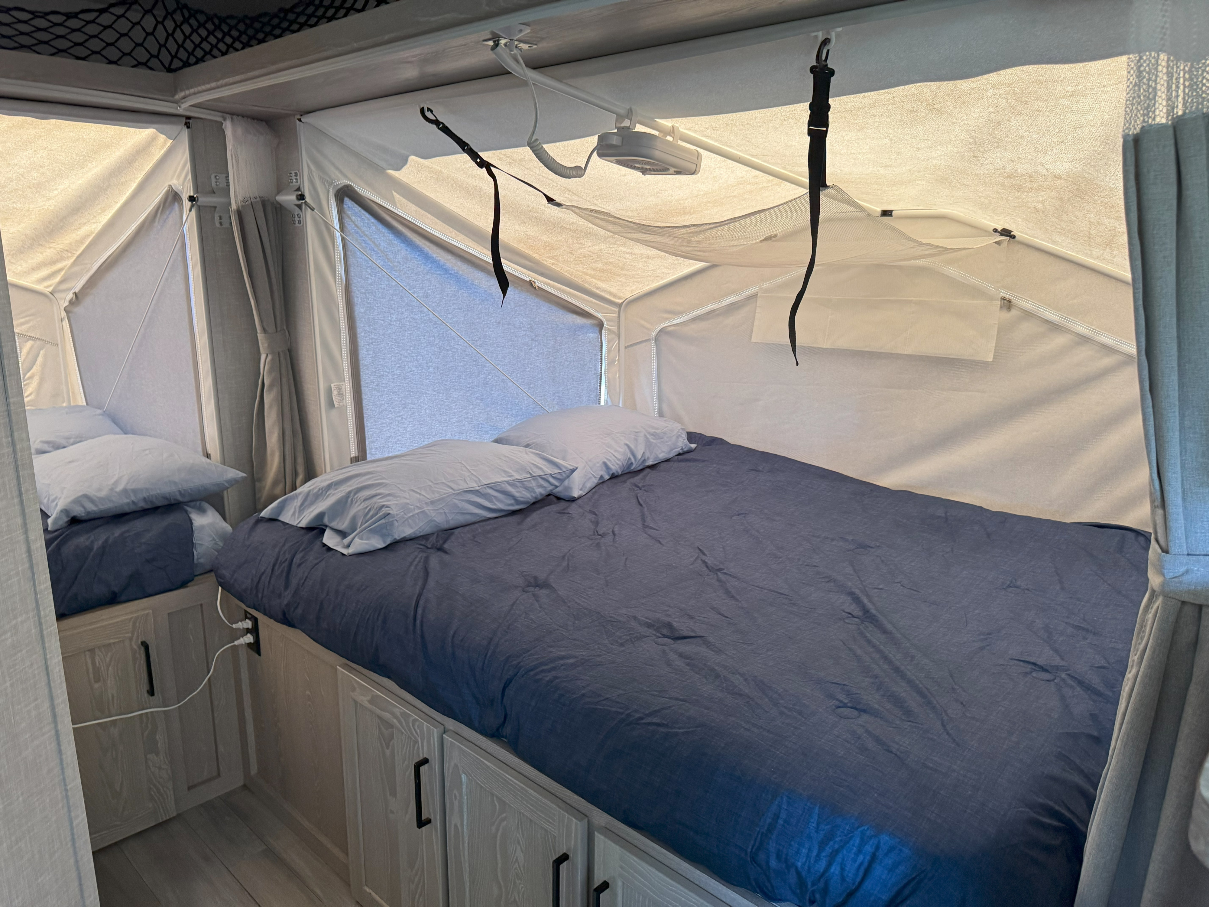Inside an RV rental pop-up camper: two beds with blue bedding, fabric tent walls, and under-bed storage cabinets.. Rockwood Roo 2022