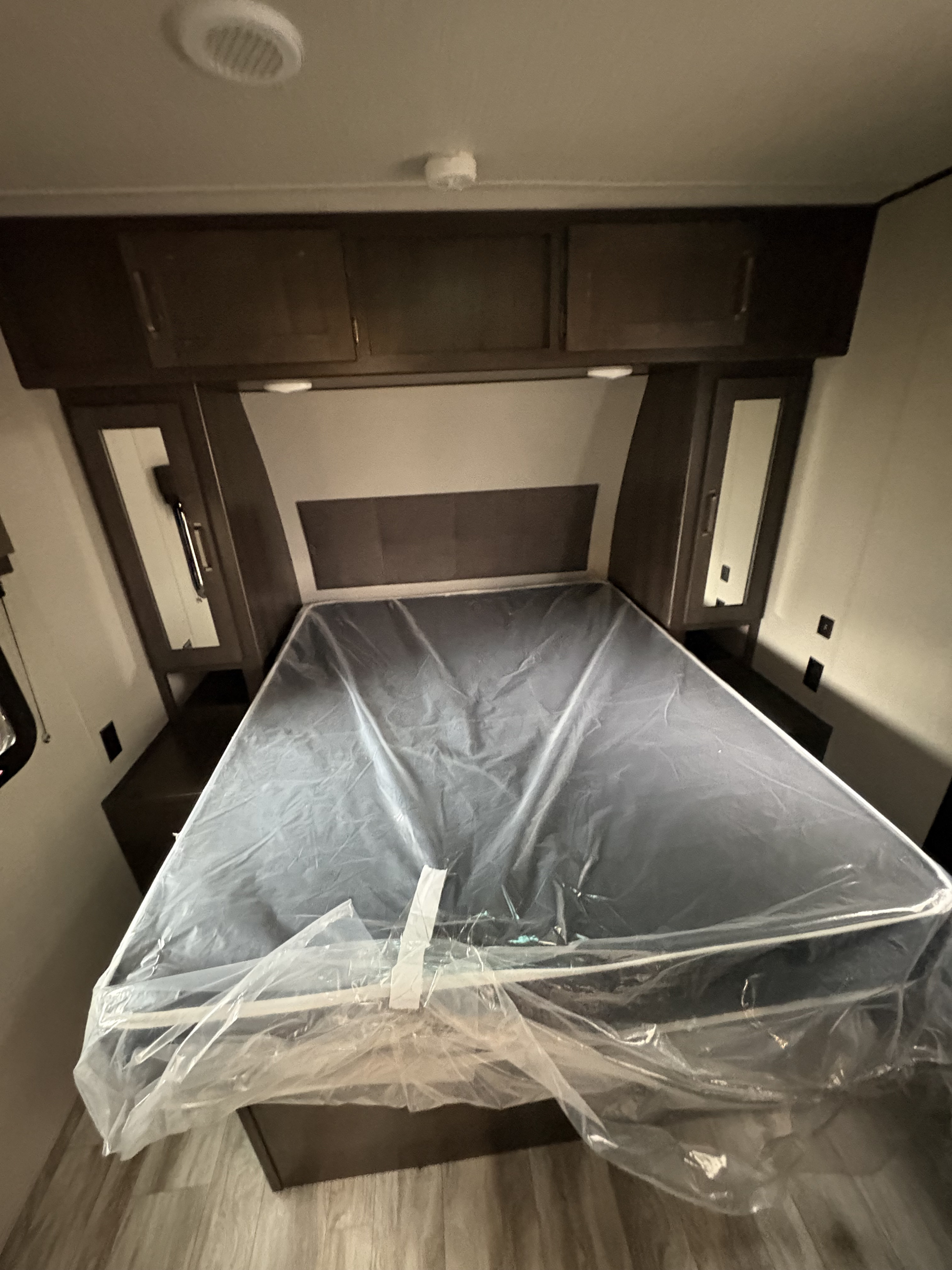 Clean RV rental bedroom with new plastic-covered mattress, overhead cabinets, and side storage, ready for your trip.. Grand Design Transcend Xplor 2022