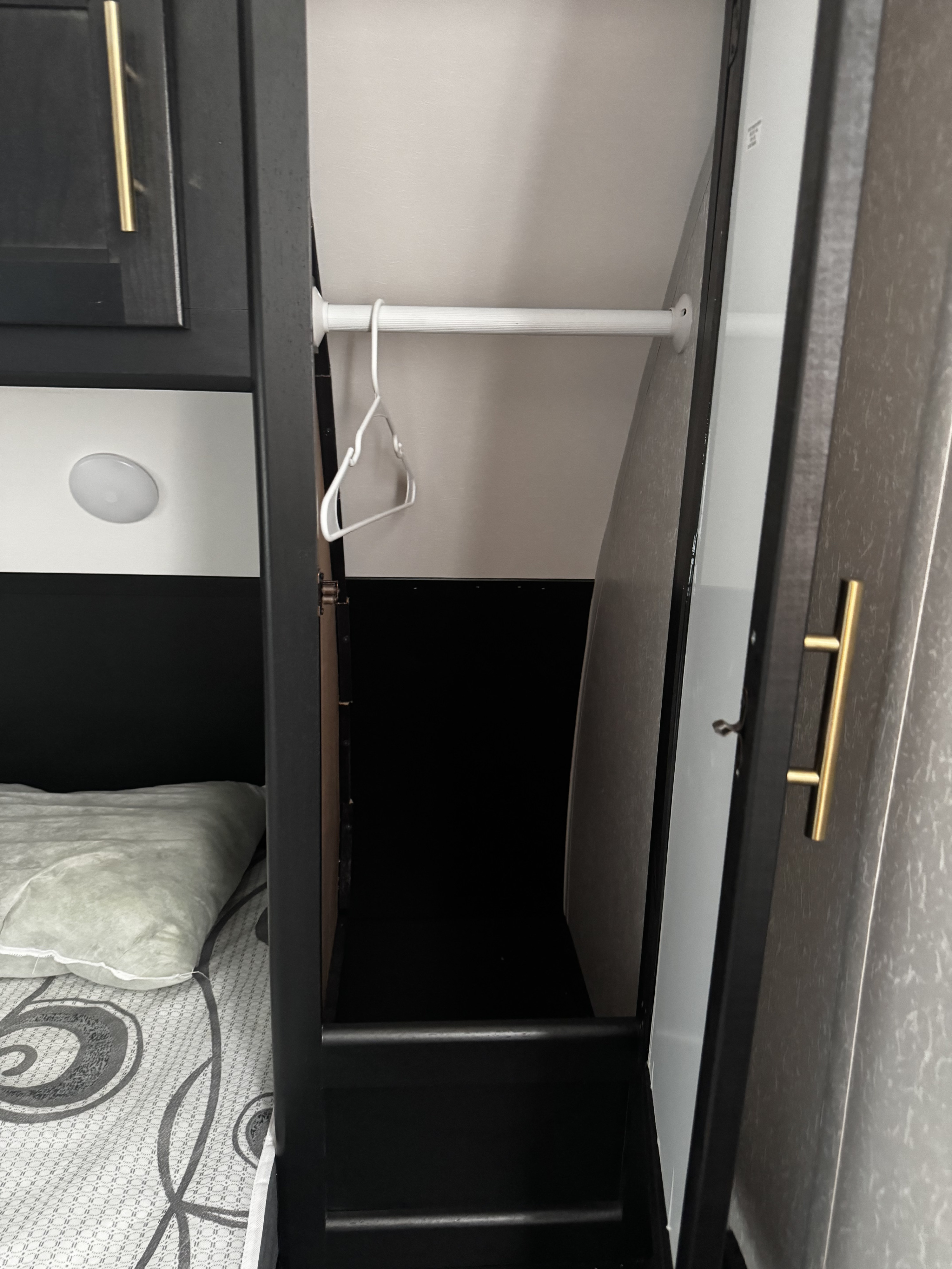 Inside an RV rental bedroom: a small closet with a hanging rod and hanger, next to a bed with a pillow and a light fixture.. Forest River Cherokee Grey Wolf 2022