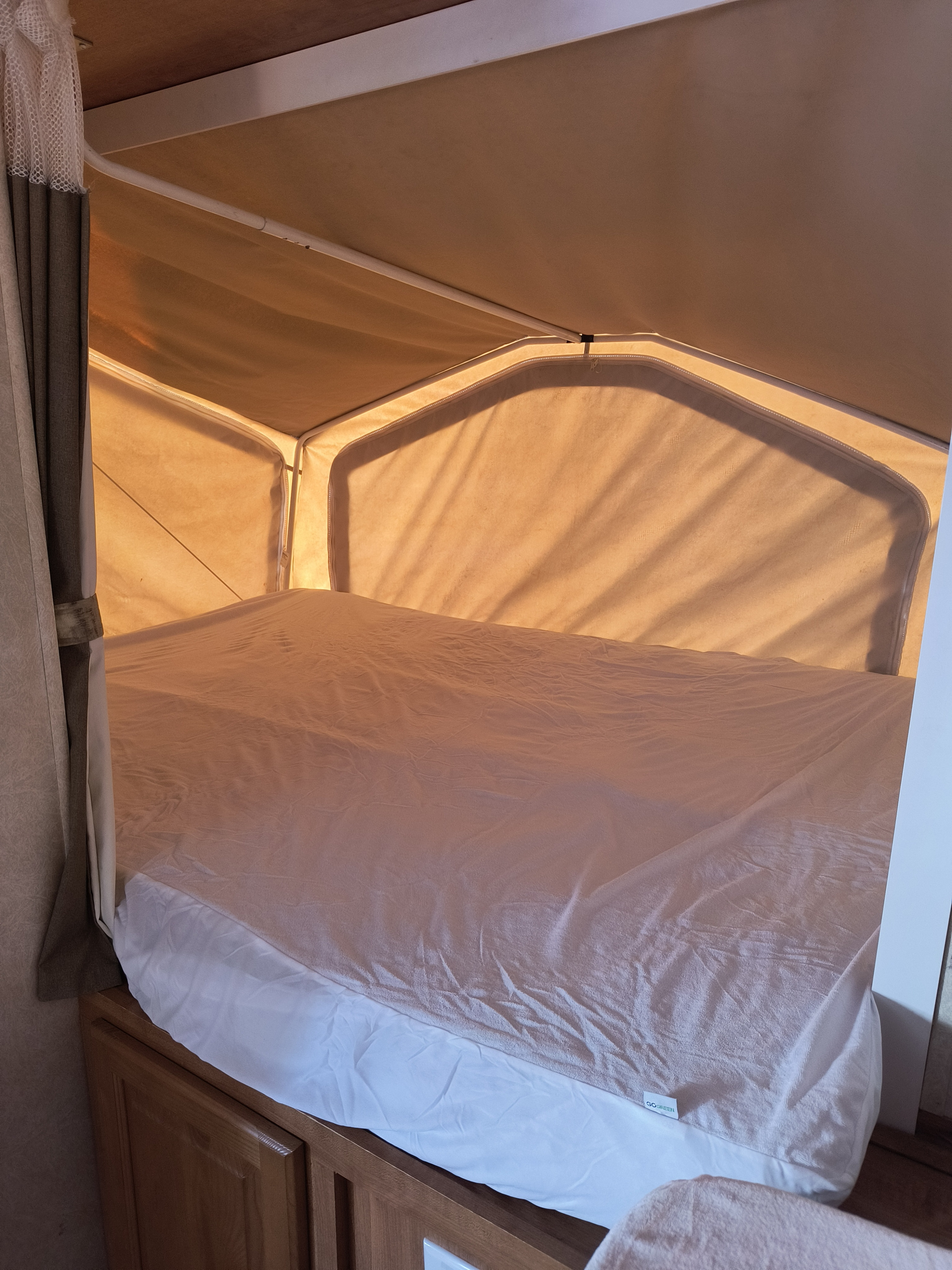 An RV rental pop-up camper bed, featuring a white sheet and textured cover, bathed in warm sunlight through canvas walls.. Forest River Flagstaff Shamrock 2009