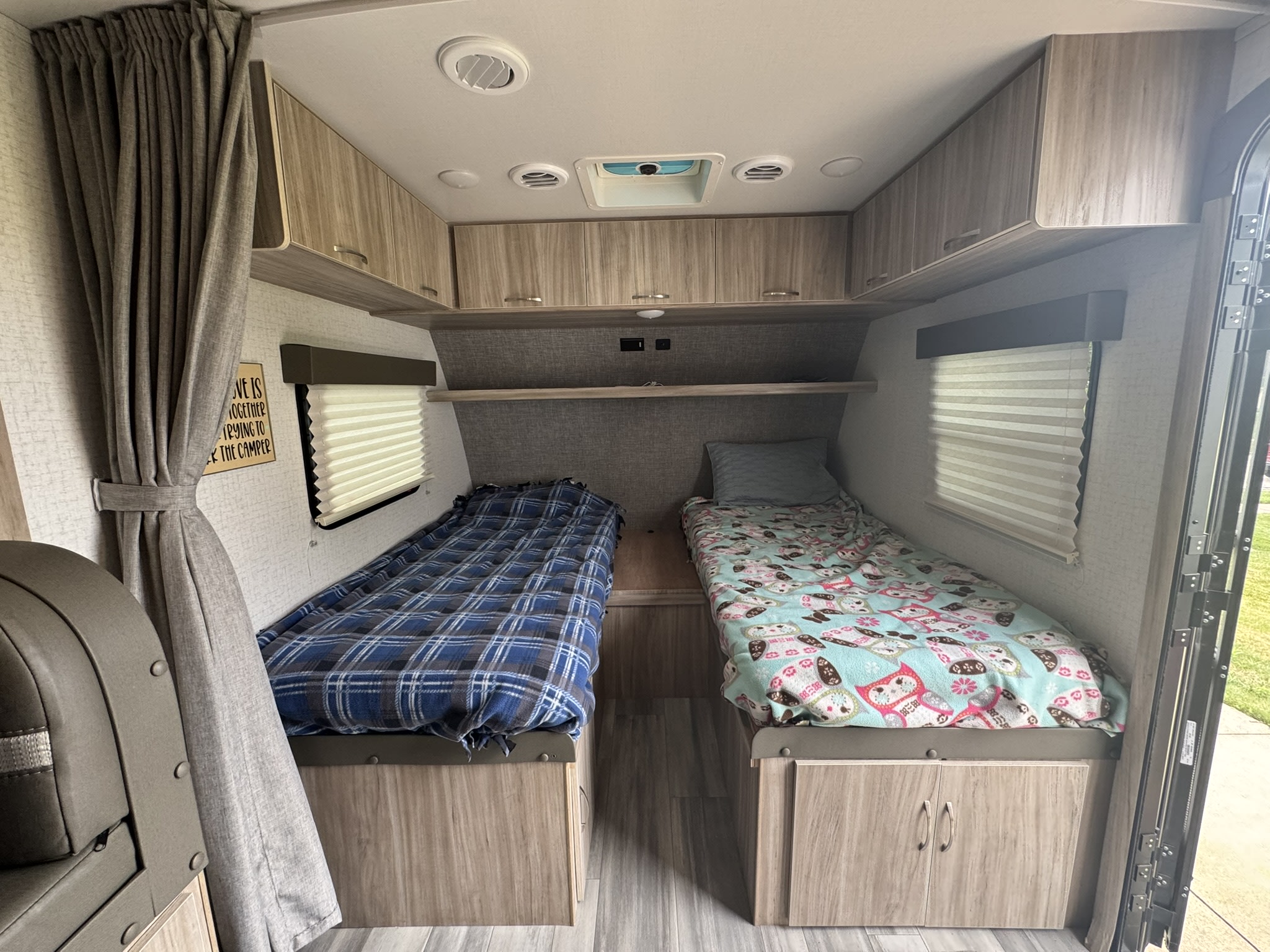 Inside a comfortable RV rental: two twin beds with blankets, overhead cabinets, and windows with blinds.. Minnie Micro Minnie 2021