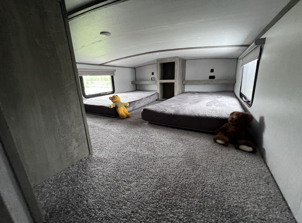 This RV rental bunk room features two floor beds with grey mattresses, a built-in cubby, and cozy carpet. Two bears rest on the beds.. Forest River Salem Hemisphere 2022