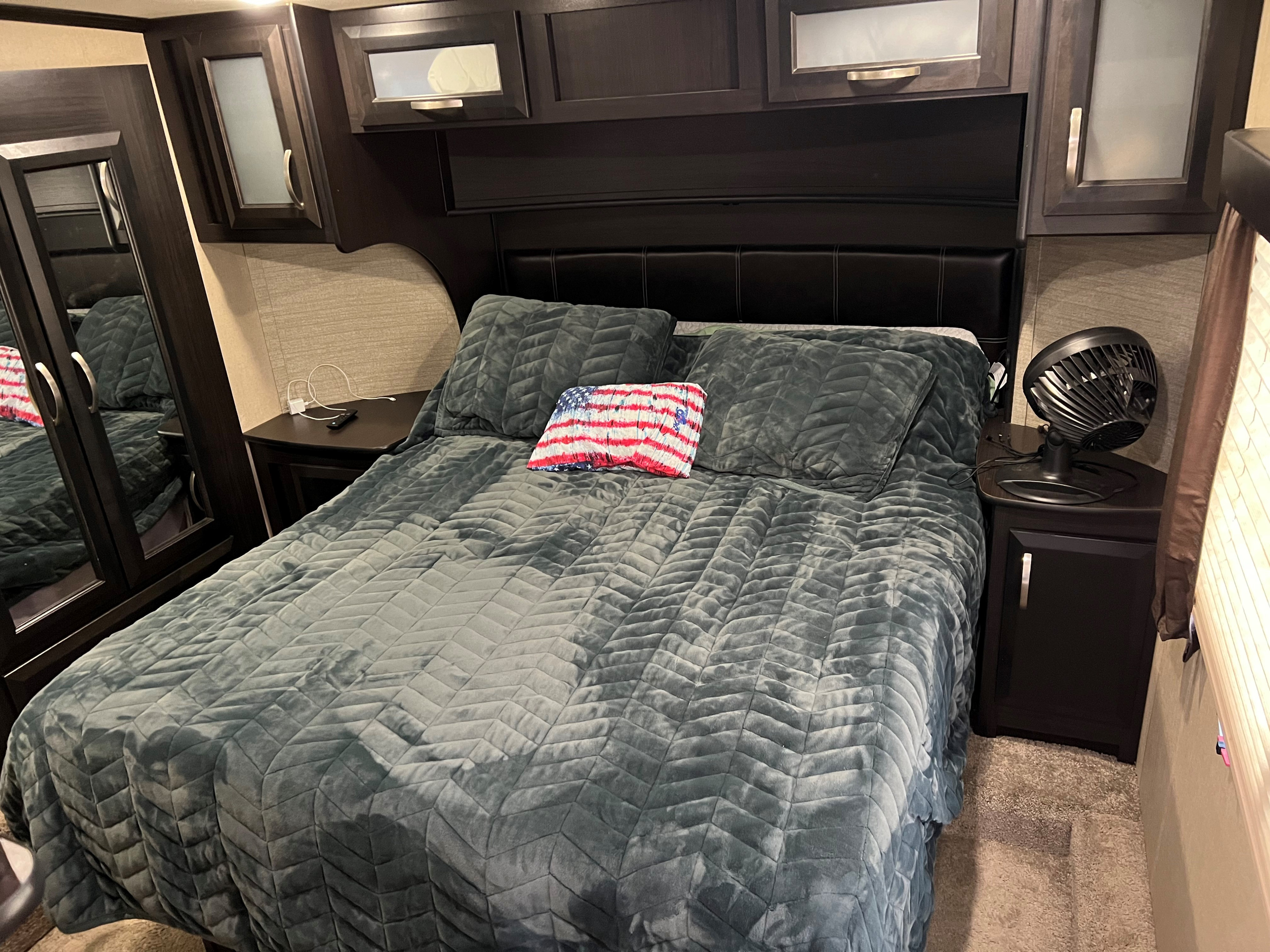 Cozy RV rental bedroom featuring a comfortable bed, overhead cabinets, and a mirrored closet, ideal for travel.. Dutchmen Voltage 2018