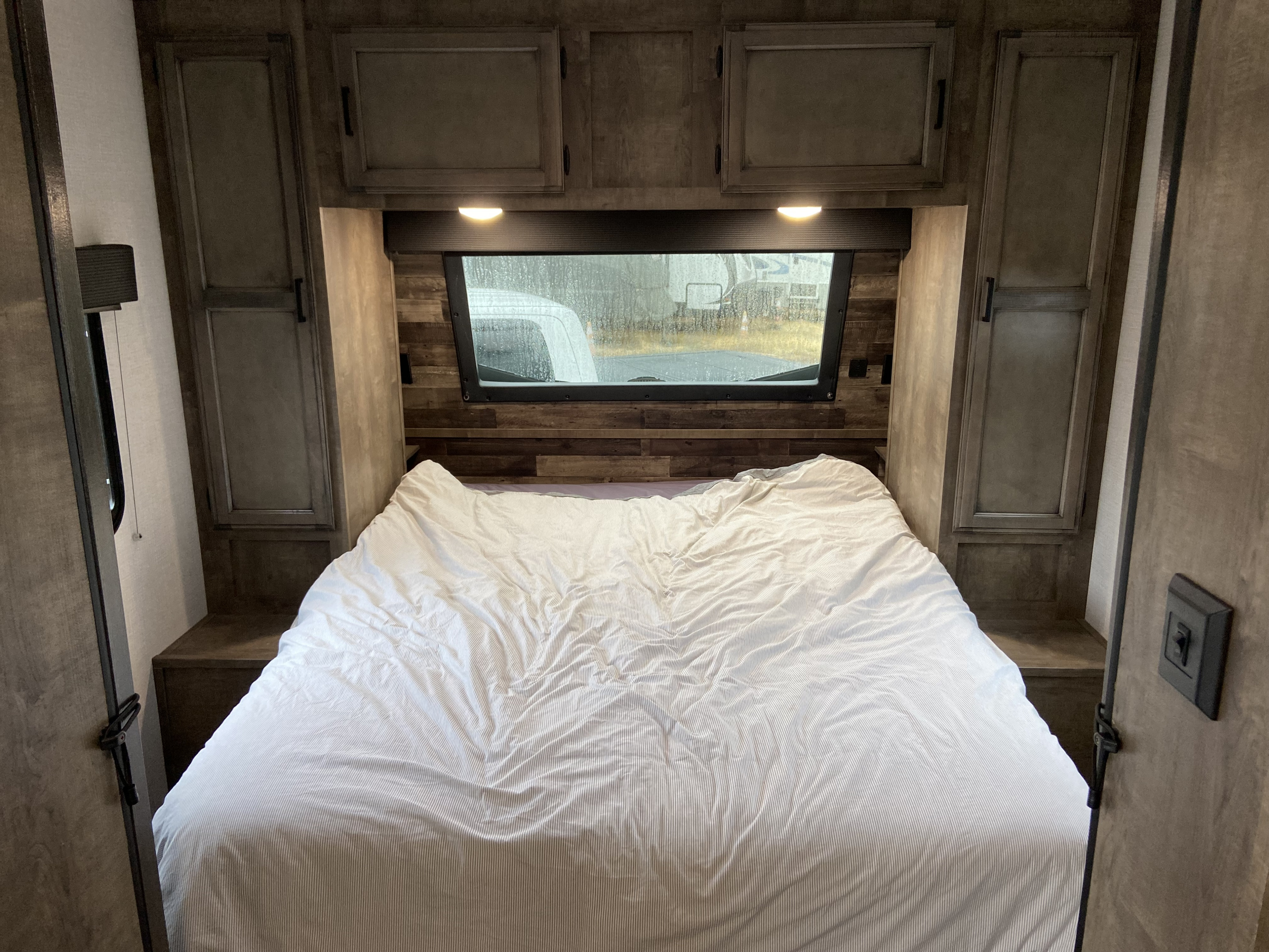 Cozy RV rental bedroom interior with storage, white striped bedding, and a window view, ideal for travel.. Venture Sport Trek 2021