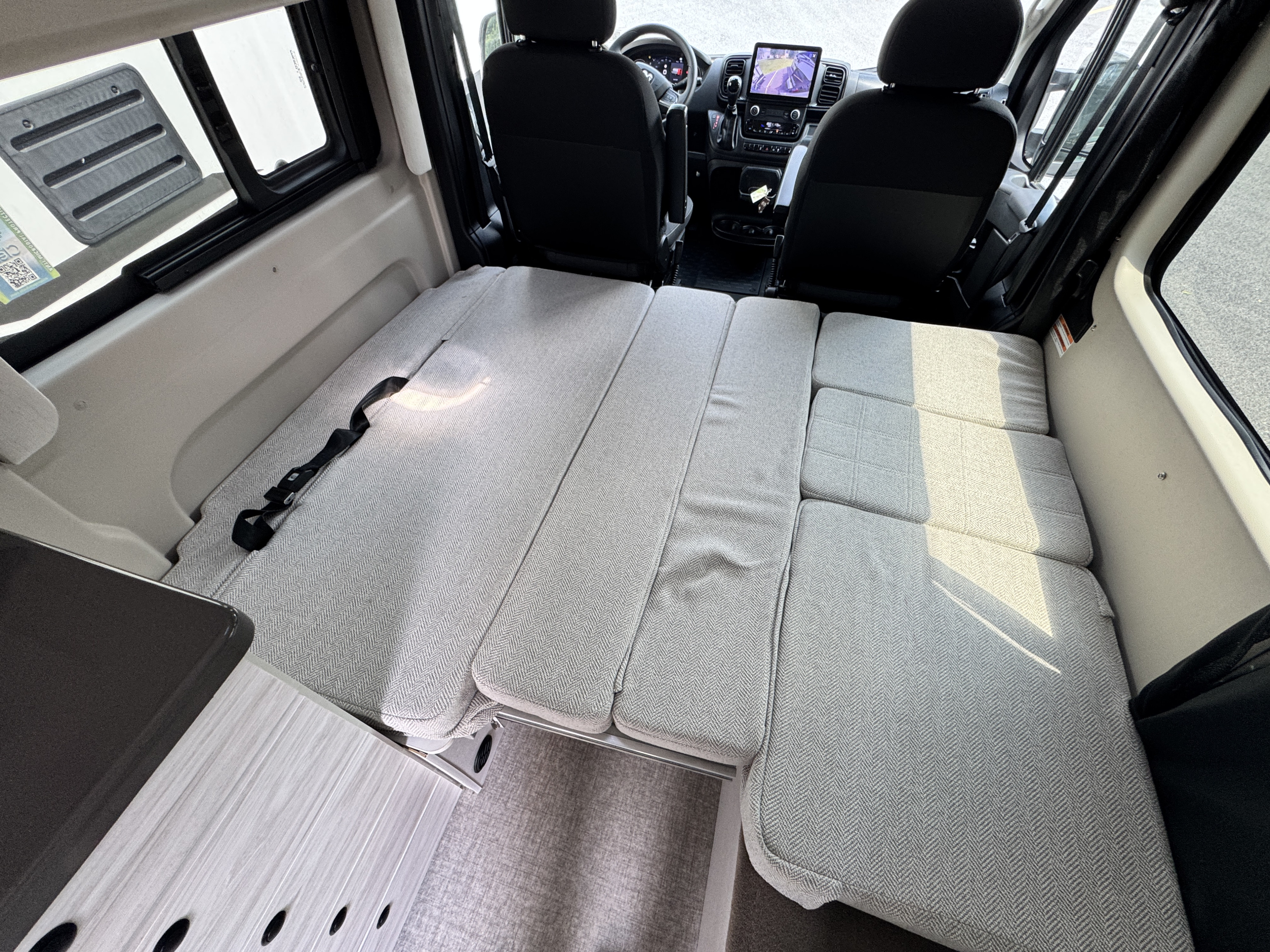 This rv rental features a convertible light grey cushion bed system. View from rear, showing cockpit and interior amenities.. Entegra Coach ARC 2024