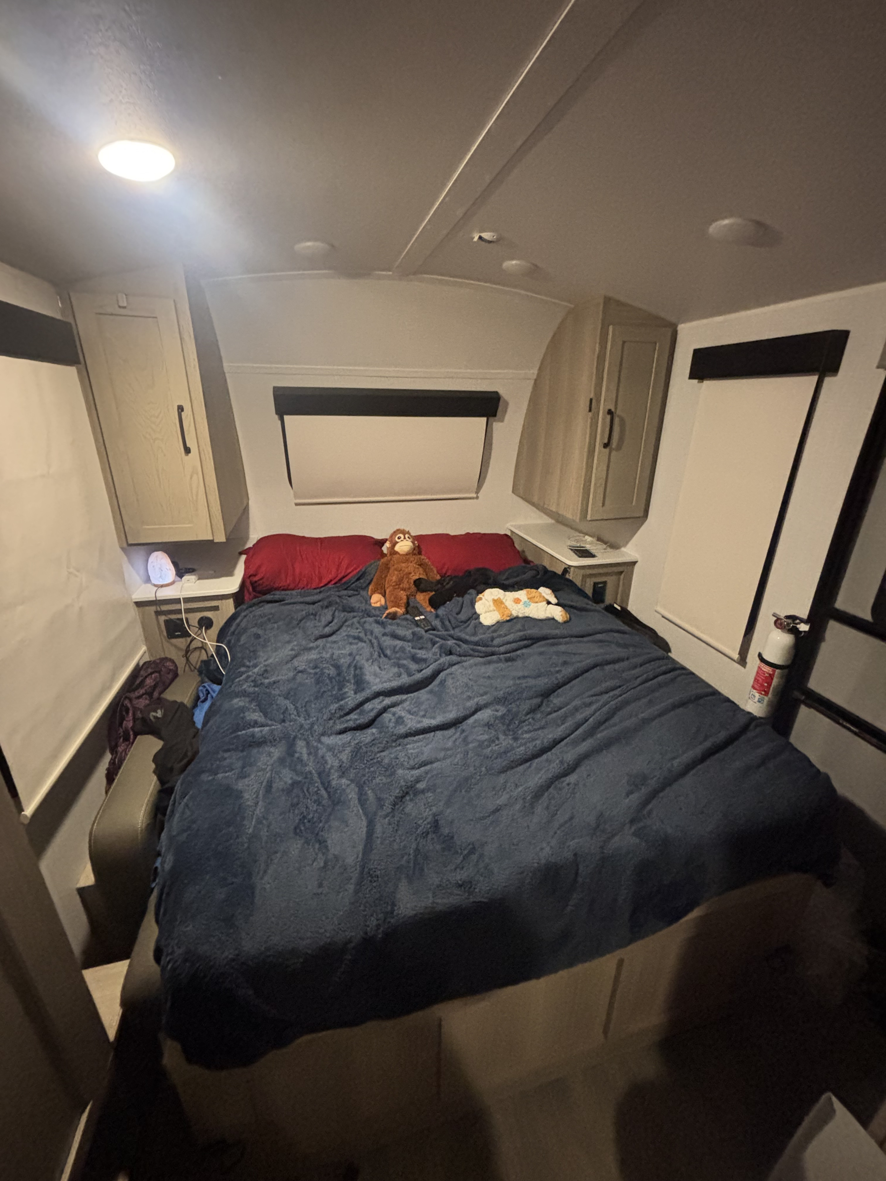 Cozy RV rental bedroom with a large bed, blue blanket, stuffed animals, overhead cabinets, and essential safety features like a fire extinguisher.. Forest River Flagstaff E-Pro 2024