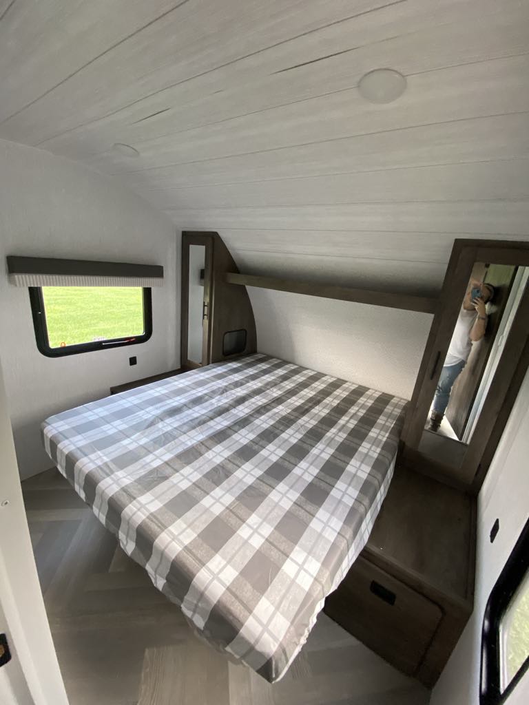 Inside an RV rental: a cozy bedroom featuring a bed with plaid cover, window, and wood-toned storage.. Forest River Salem Cruise Lite 2022