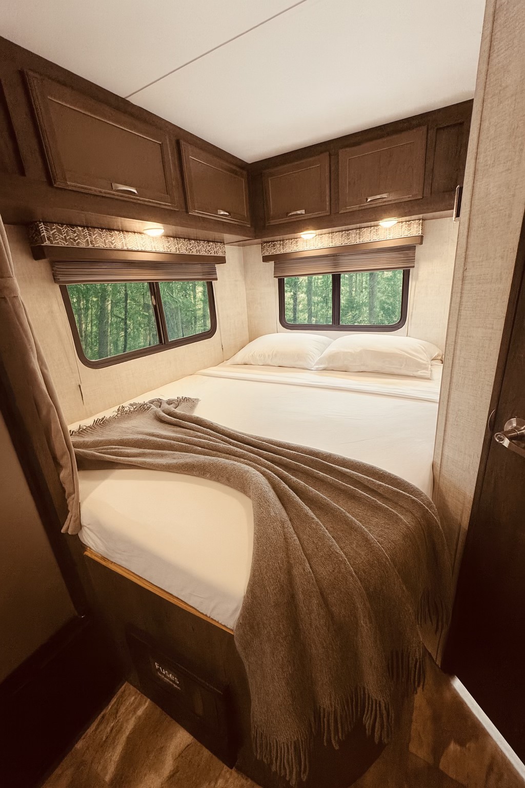 Cozy RV rental bedroom featuring a bed with white bedding, throw blanket, overhead cabinets, and tranquil forest views.. Gulf Stream Conquest 2023