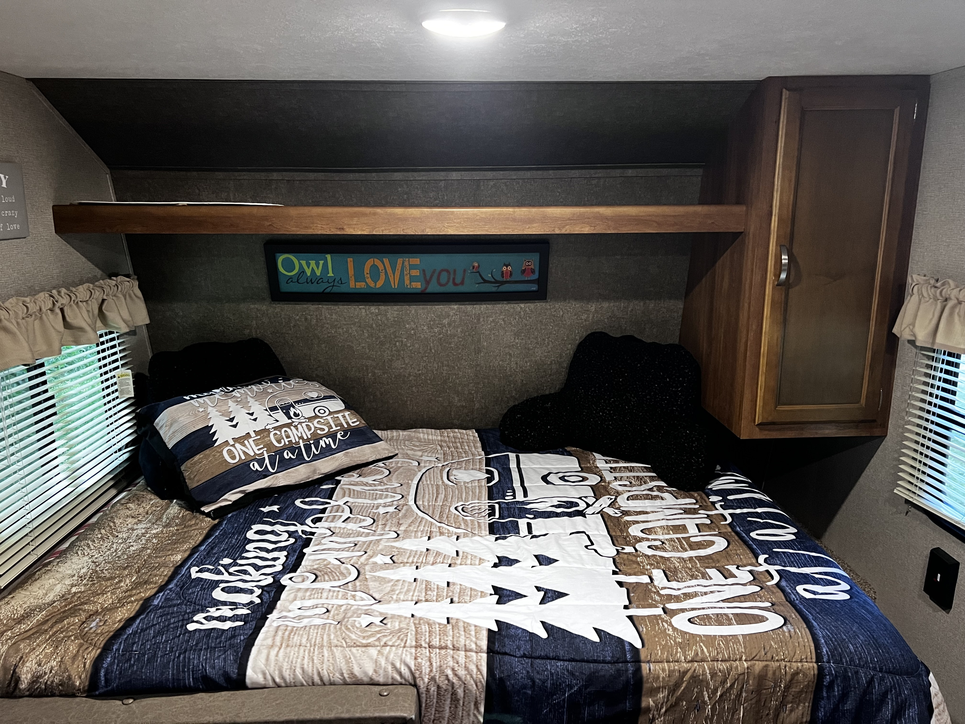 Interior of an RV rental bedroom showing a comfortable bed with camping-themed bedding and overhead storage.. Keystone RV Summerland Mini 2017