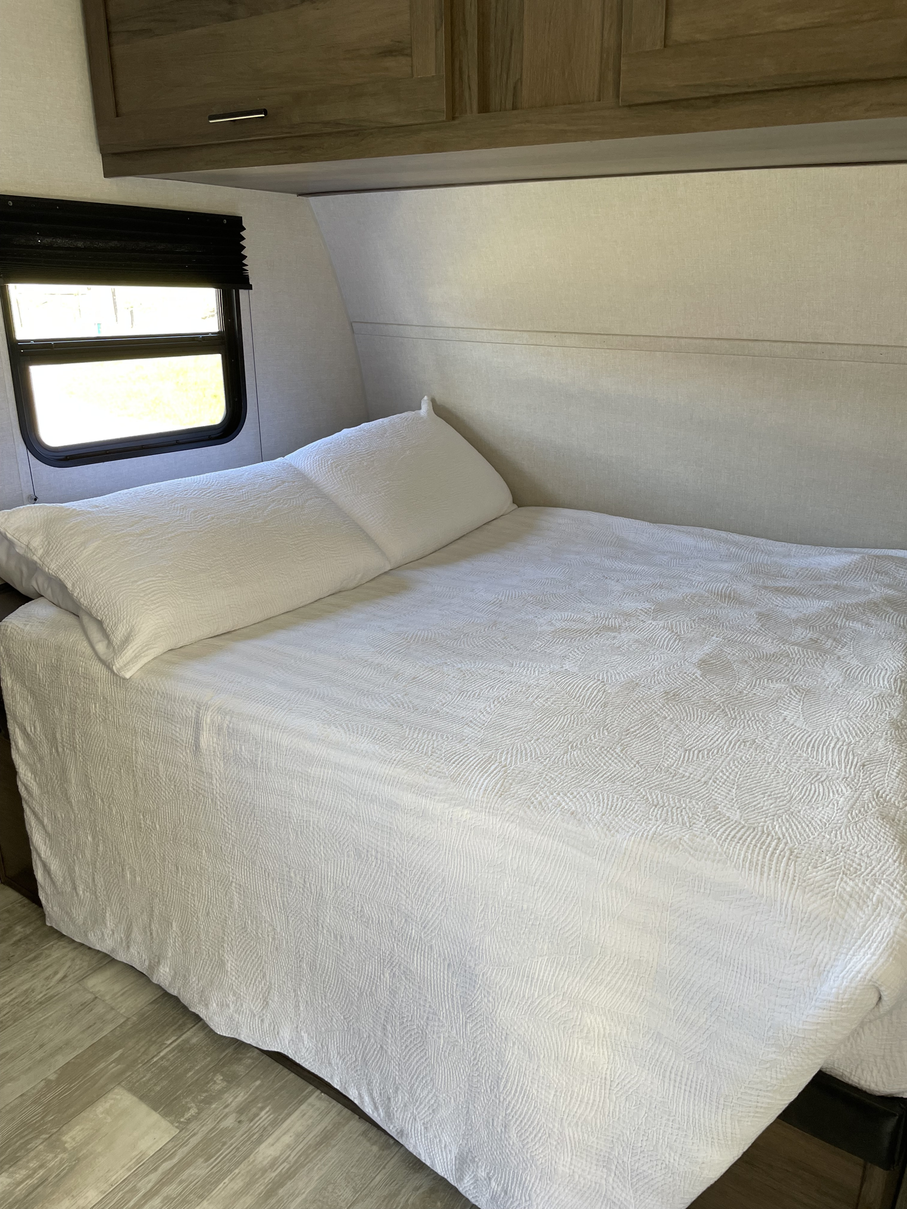 RV rental interior: Clean white bed with textured bedding, window, and overhead cabinets in a comfortable bedroom space.. Avenger LT 2021