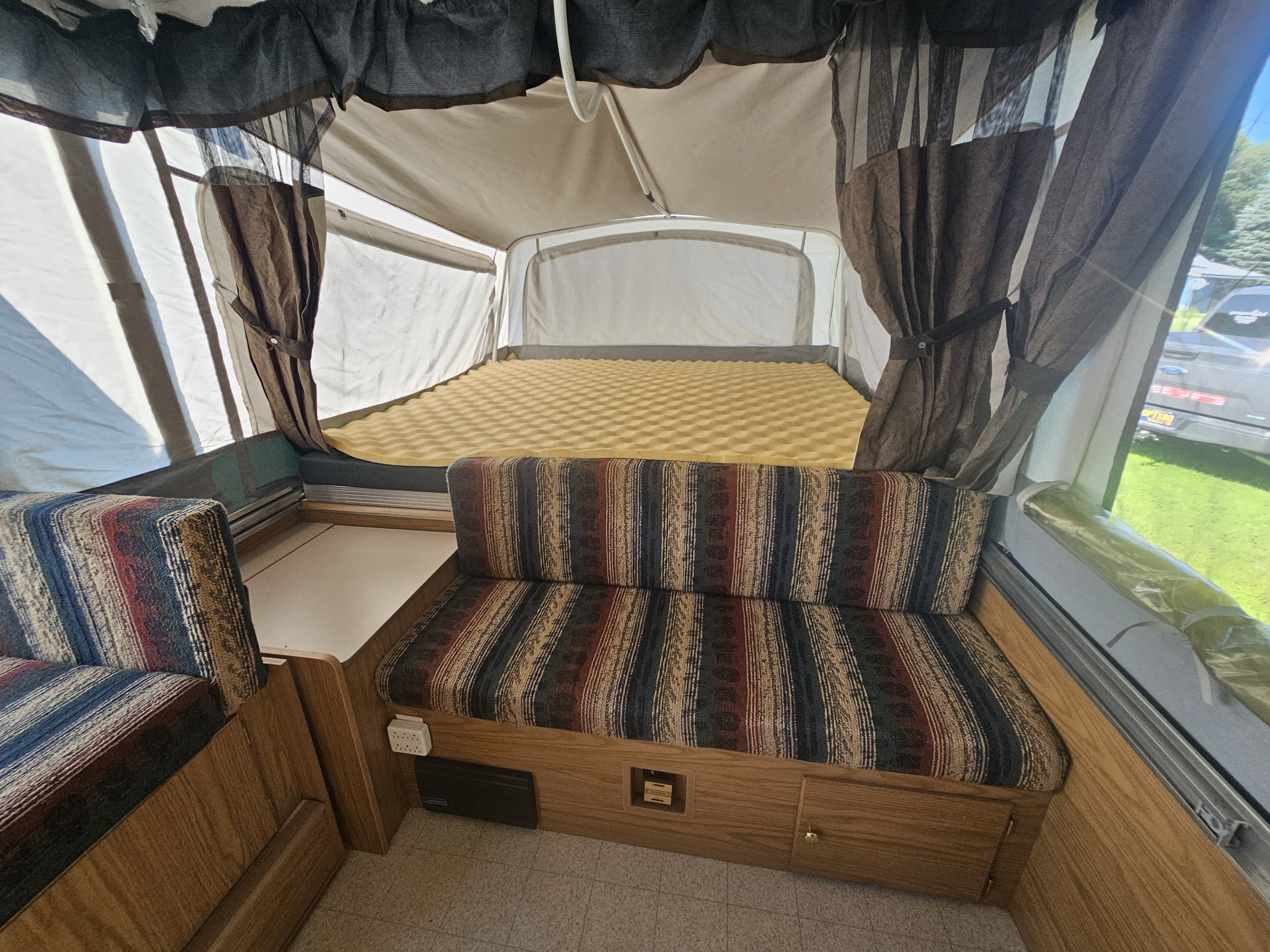 Interior of a pop-up RV rental, featuring a comfortable bed, striped bench seating, and curtained windows.. Coleman Destiny 2000