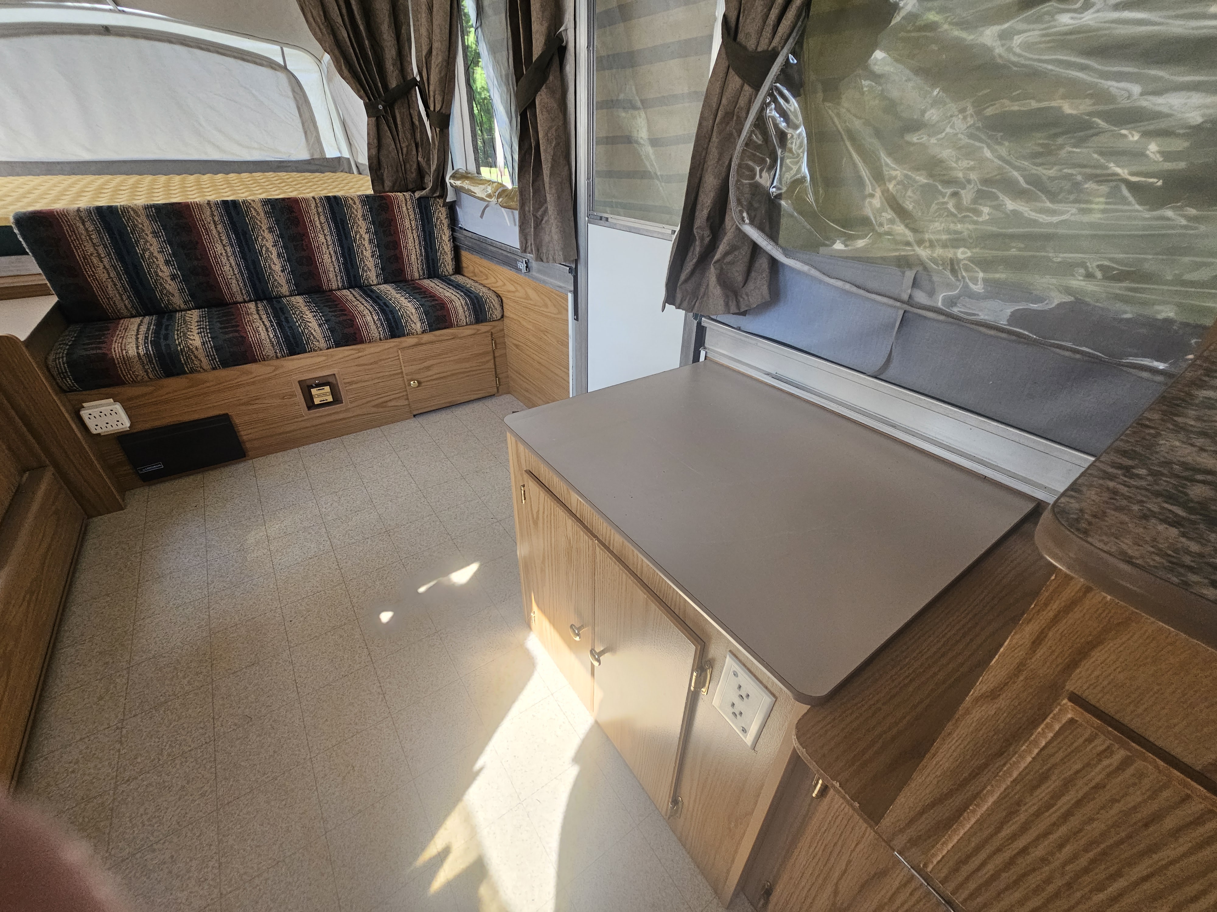 Cozy pop-up camper interior for RV rental. Features a patterned sofa, bed, and compact kitchenette. Bright vinyl floor visible.. Coleman Destiny 2000