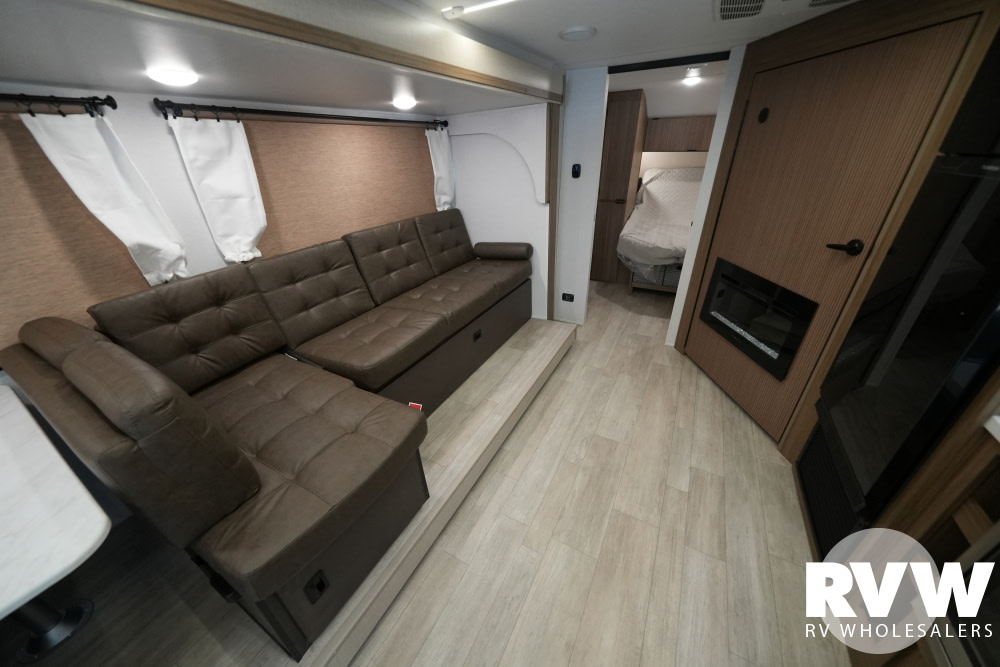 Spacious RV rental interior with an L-shaped sofa, light wood flooring, and bedroom access. Features a cozy fireplace.. Forest River Wildwood X-Lite 2025