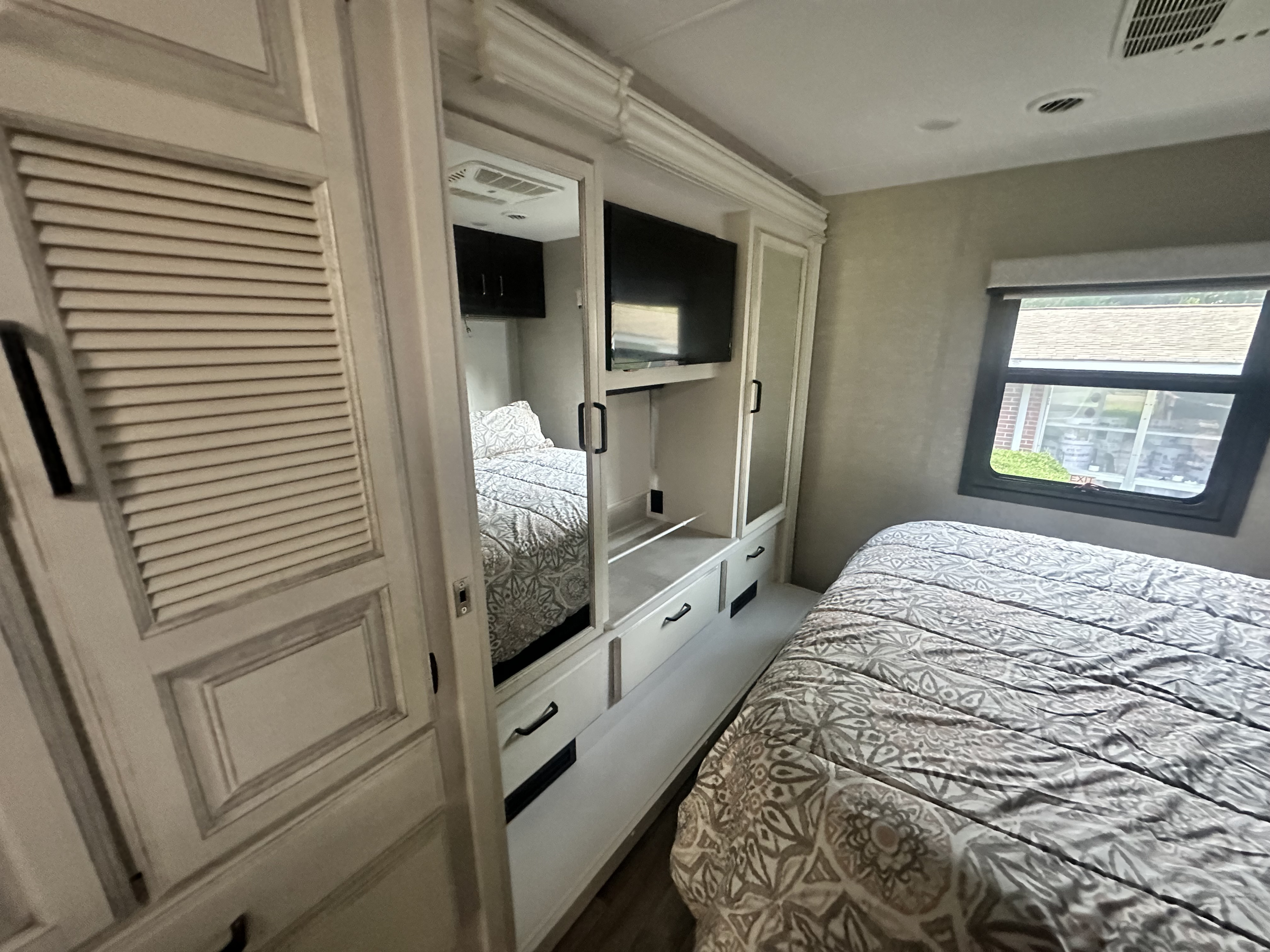 Comfortable RV rental bedroom featuring a patterned bed, built-in storage with TV, and a window view.. Jayco Precept Prestige 2022