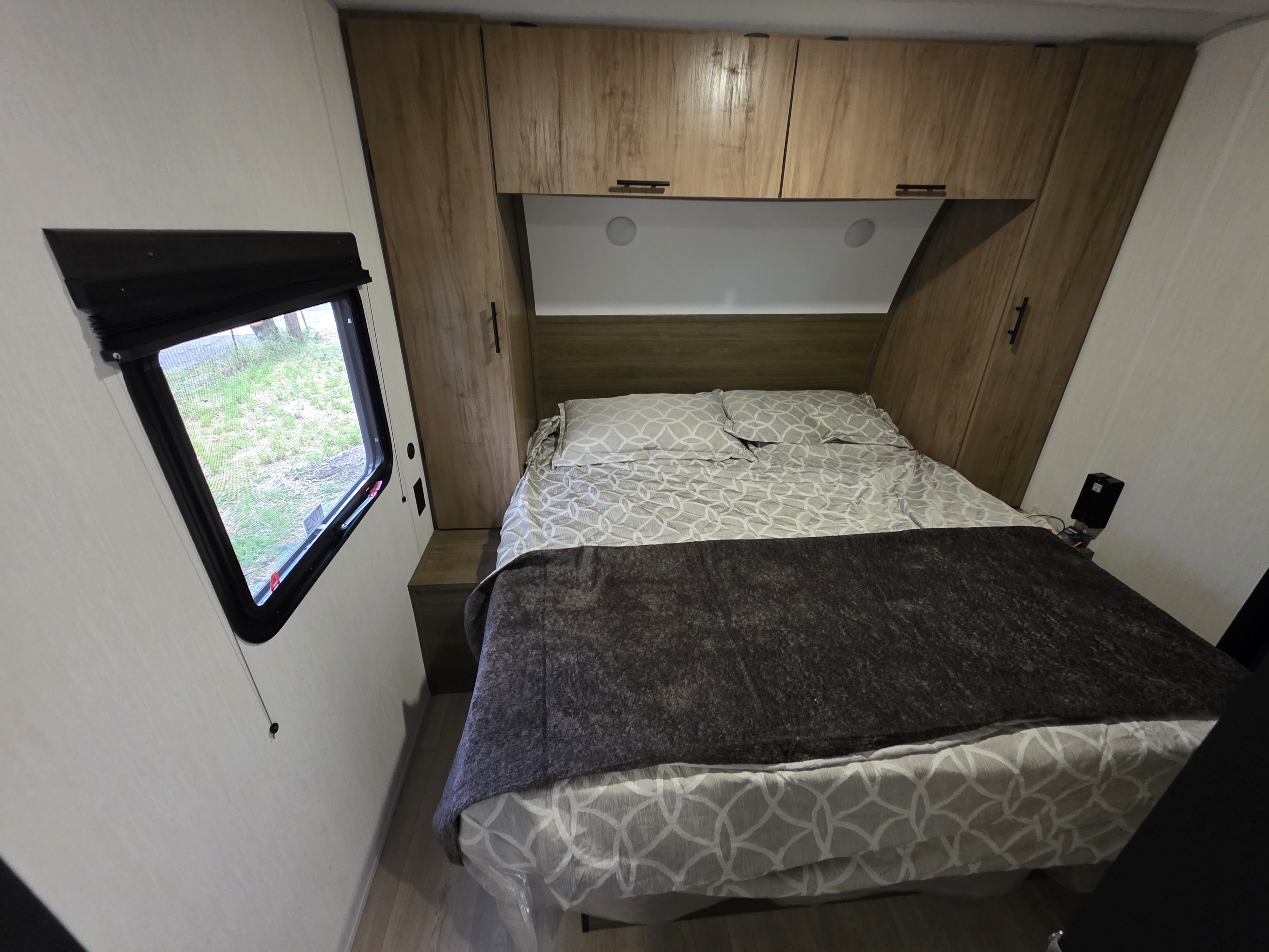Cozy RV rental bedroom featuring a comfortable bed, overhead cabinets, and a large window looking out onto greenery.. 4x4tcke22sk092479 Forest River Cherokee 2025