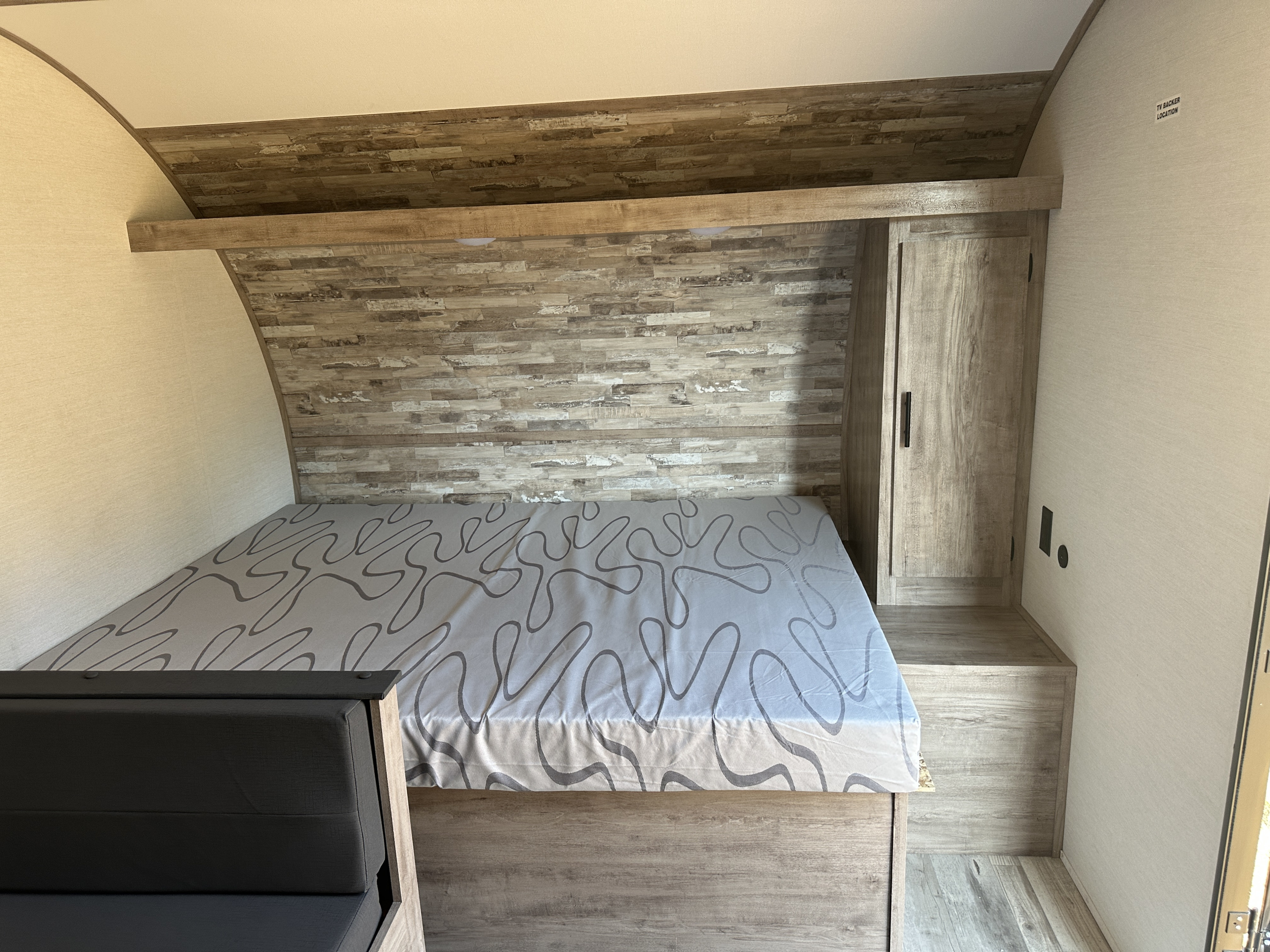 Cozy RV rental bedroom featuring a grey patterned mattress on a wooden base, wood-paneled wall, built-in wardrobe, and black seating.. Gulf Stream Enlighten 2025