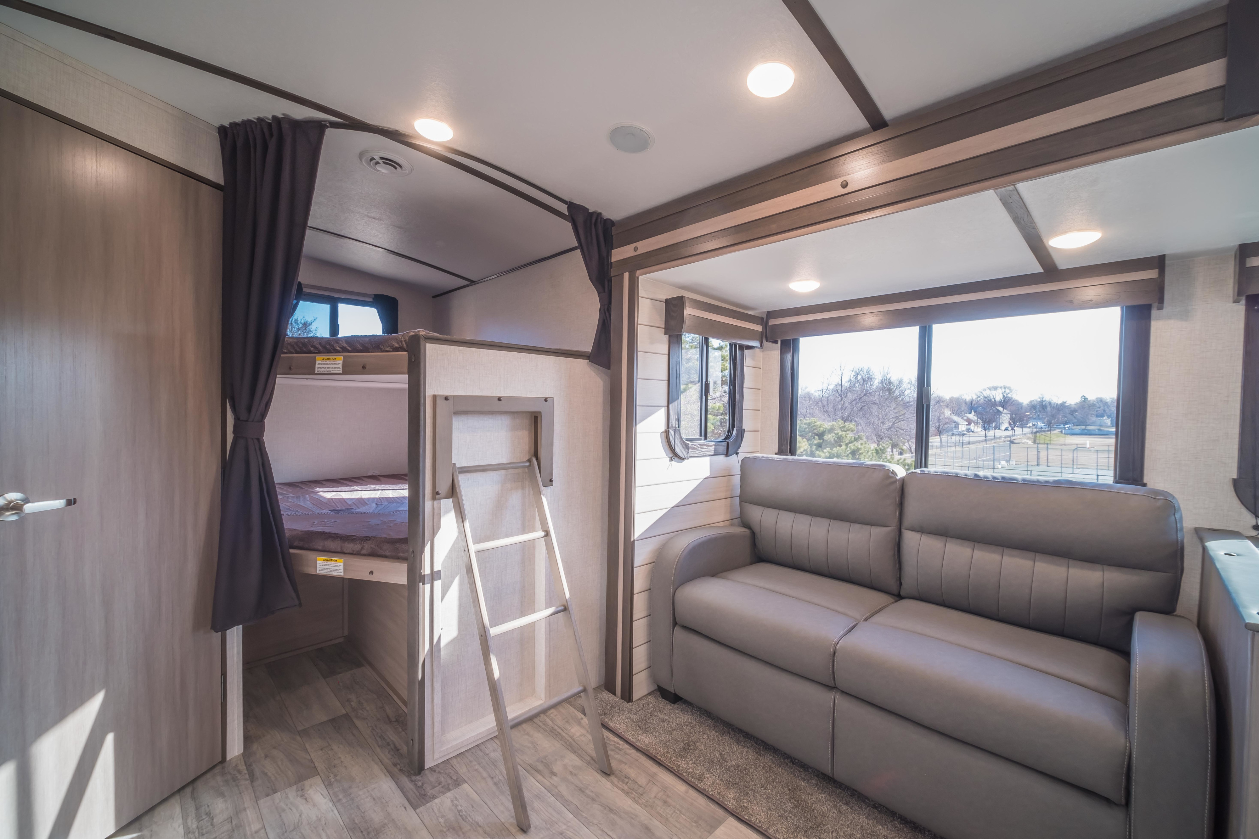 This modern RV rental features a comfortable sofa, large windows, and separate bunk beds, creating a spacious living area.. Crossroads RV Sunset Trail Super Lite 2021