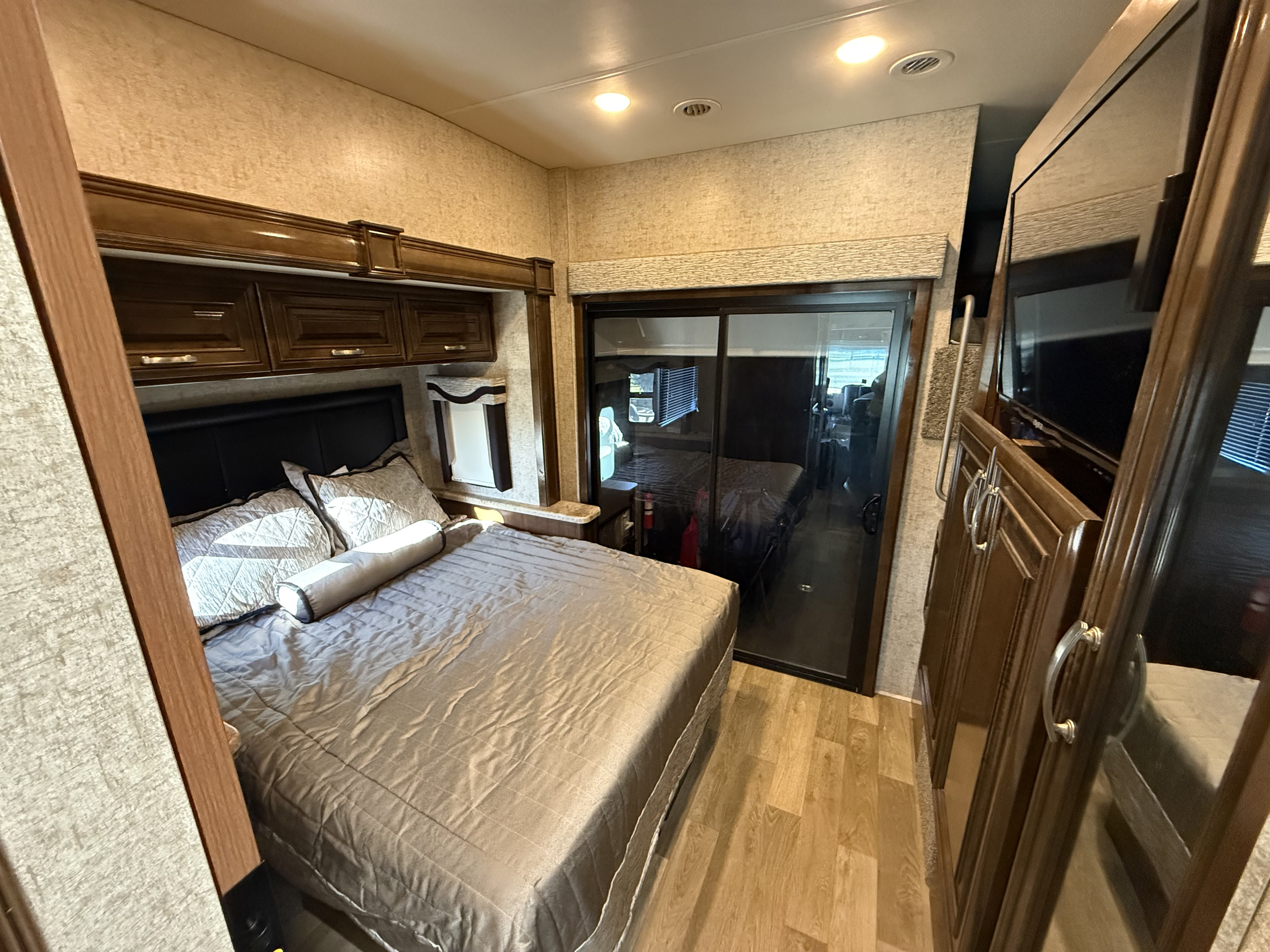 Spacious RV rental bedroom with a comfortable bed, overhead wood cabinets, and a sliding glass door to another area.. Thor Outlaw 2019
