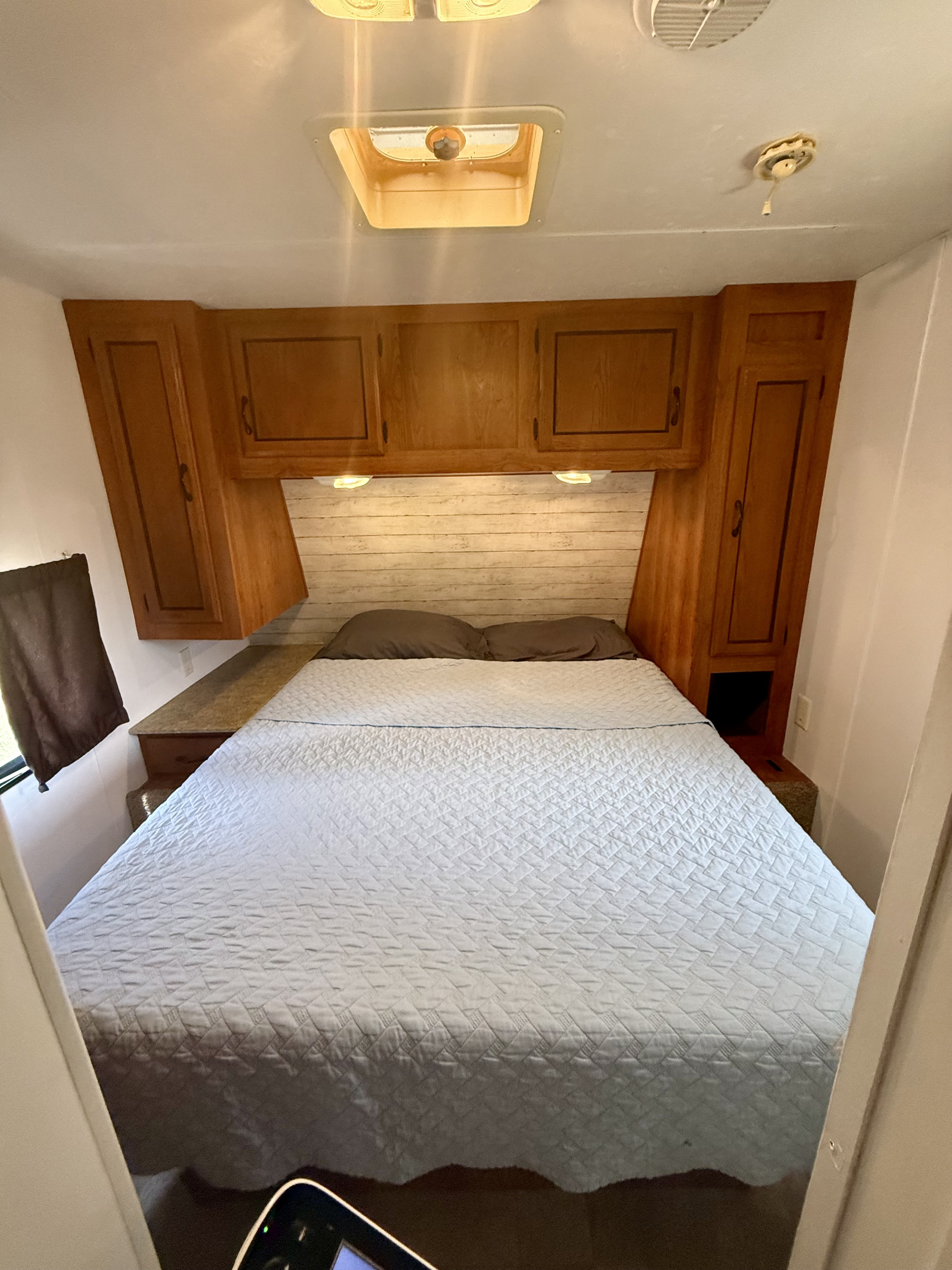 Cozy RV rental bedroom featuring a full bed with a quilted spread, overhead storage cabinets, and a shiplap headboard.. Forest River Coachmen Catalina 2010