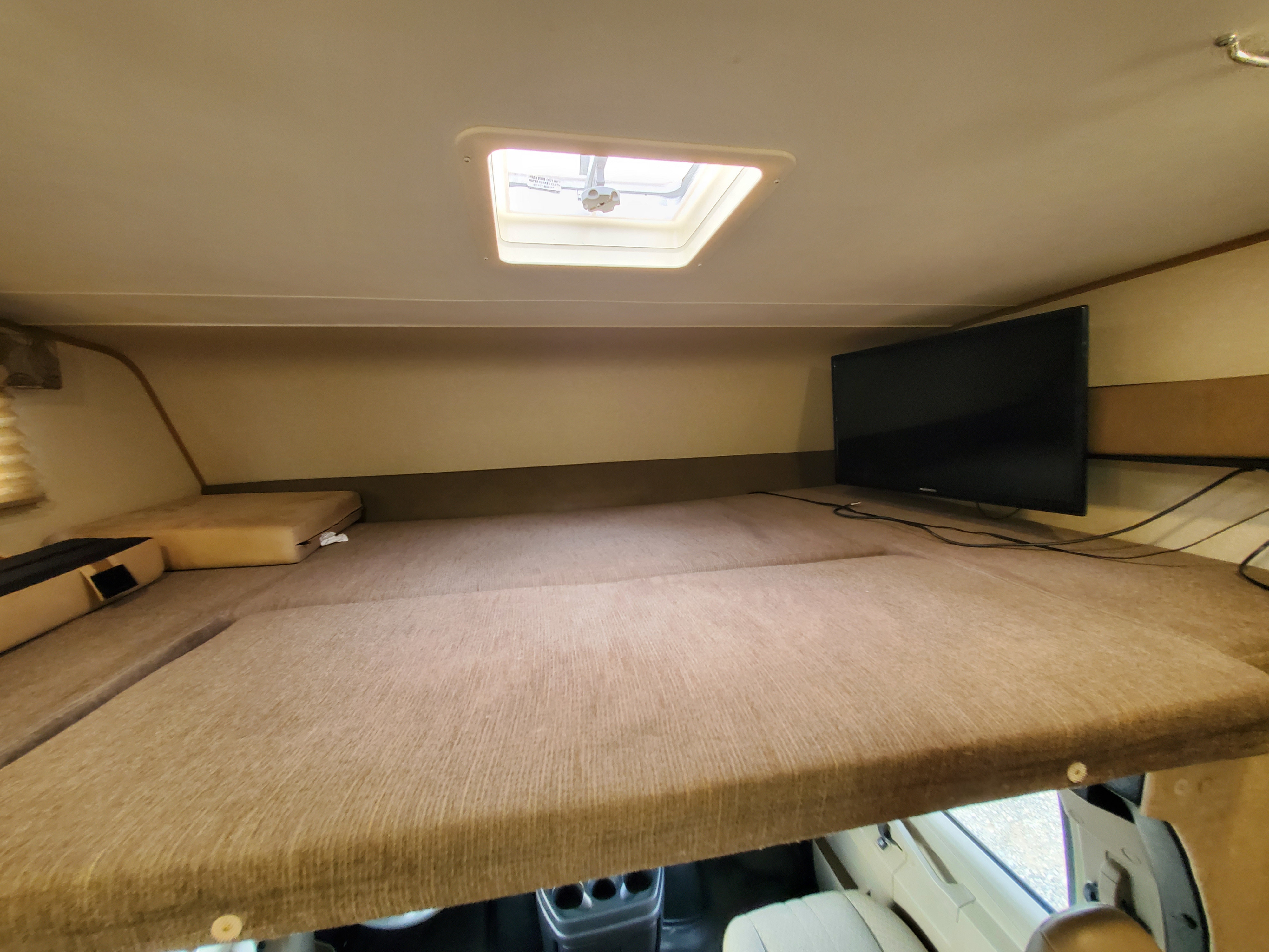 Cozy rv rental over-cab sleeping area with a skylight, comfortable mattress, and wall-mounted TV for a relaxing trip.. Coachmen Freelander 2018