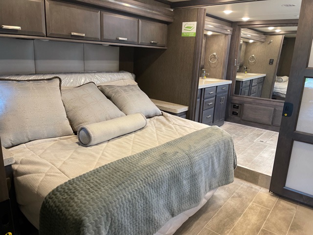 Comfortable RV rental bedroom with overhead cabinets, leading to a modern tiled bathroom with vanity and mirror.. Thor Tuscany 2022