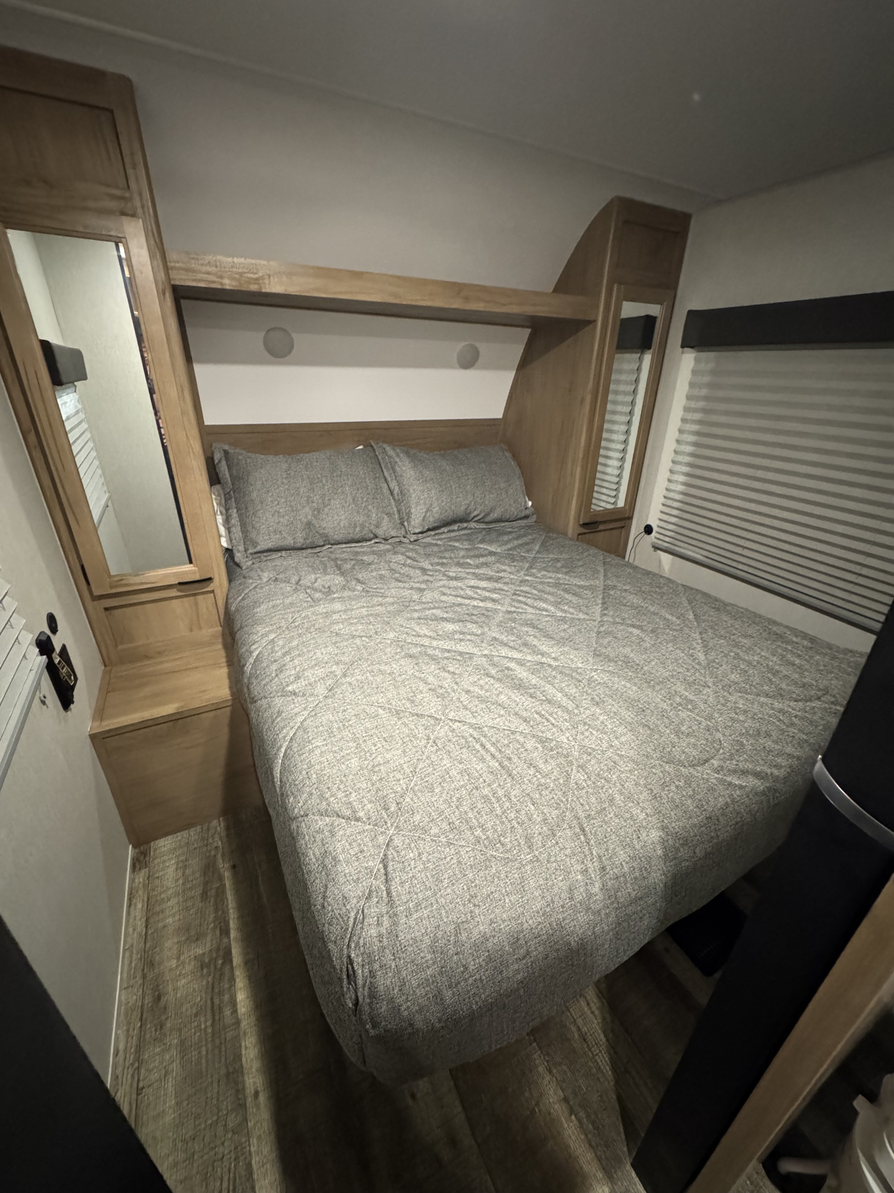 RV rental bedroom: Features a gray bed, integrated wooden headboard with mirrors, side storage, and a window with blinds.. Forest River Cherokee Grey Wolf 2024