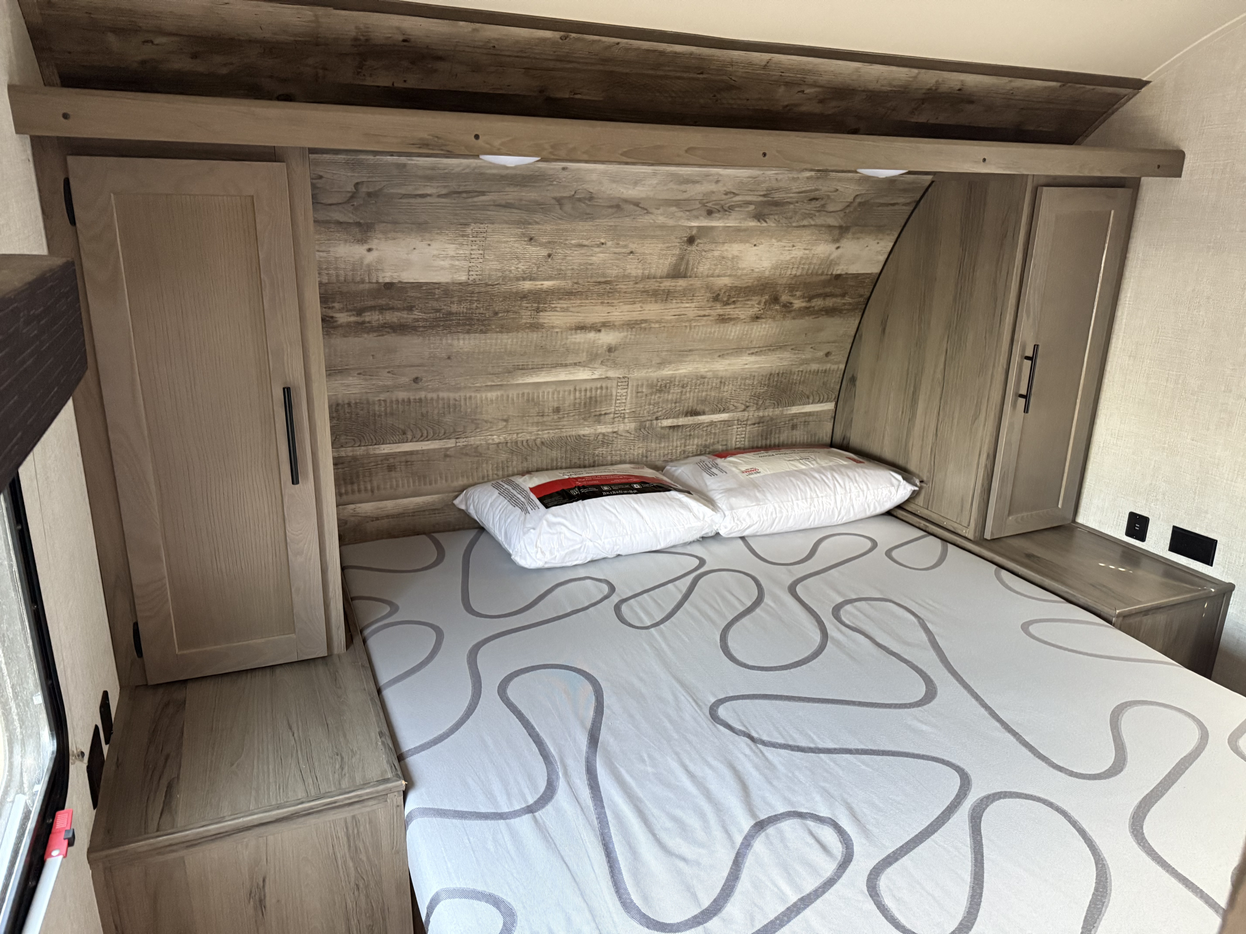 Explore this comfy RV rental bedroom: bed with squiggly pattern, rustic wood headboard, cabinets, and outlets.. Forest River Grand River 32BHS Ultralite 2022
