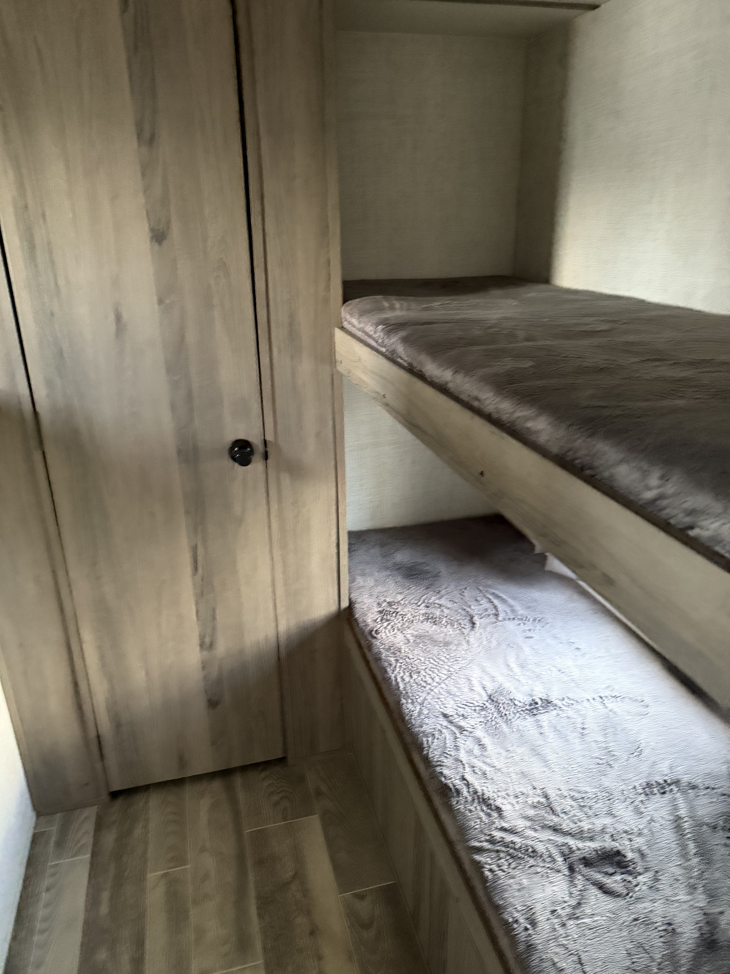 RV rental interior featuring cozy bunk beds with soft grey mattresses and a wood-paneled wardrobe, ideal for sleeping.. Forest River Grand River 32BHS Ultralite 2022