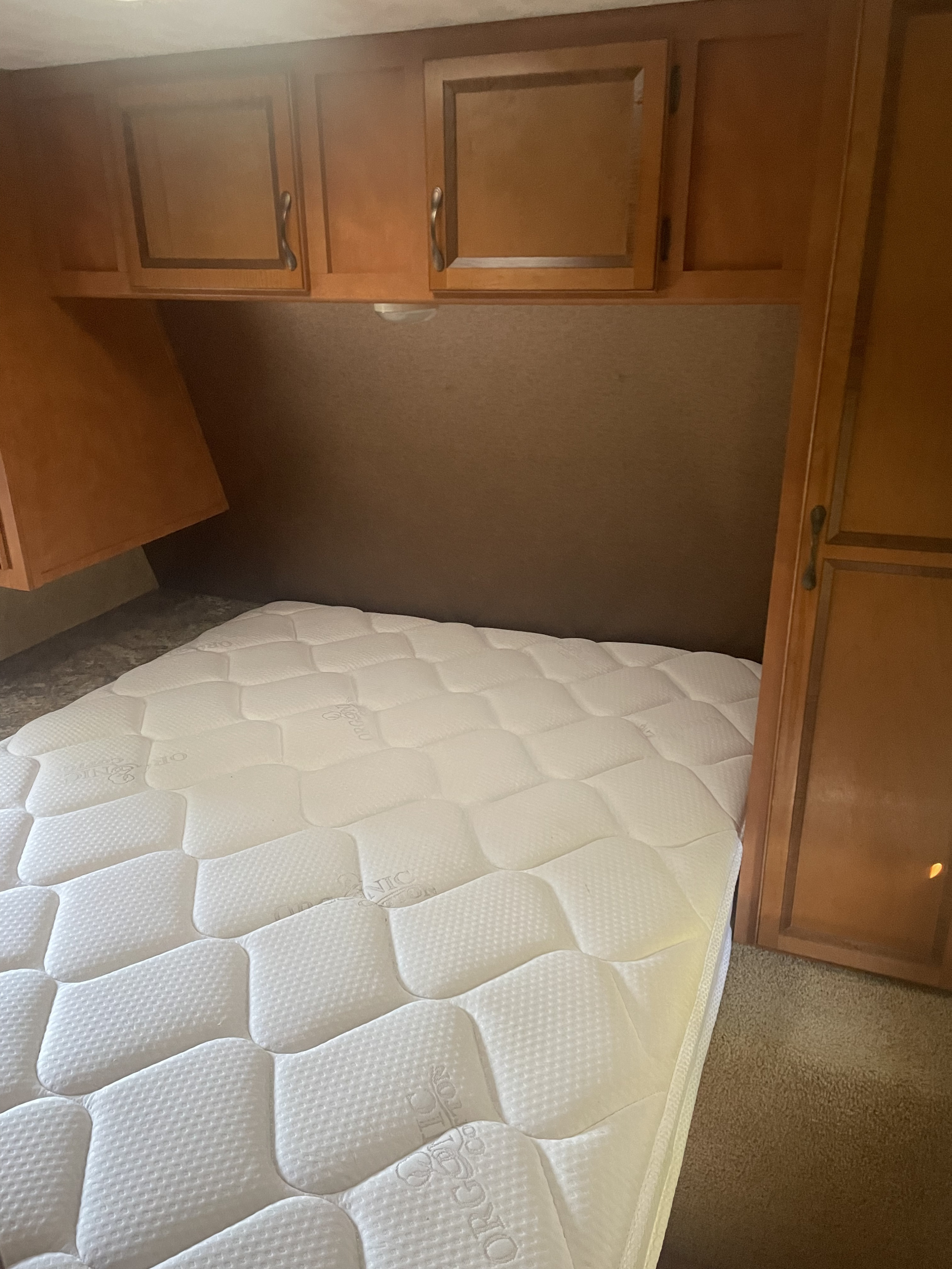 Cozy RV rental bedroom featuring a clean white mattress, overhead wooden cabinets, and brown carpeted floor.. Gulf Stream Conquest 2014